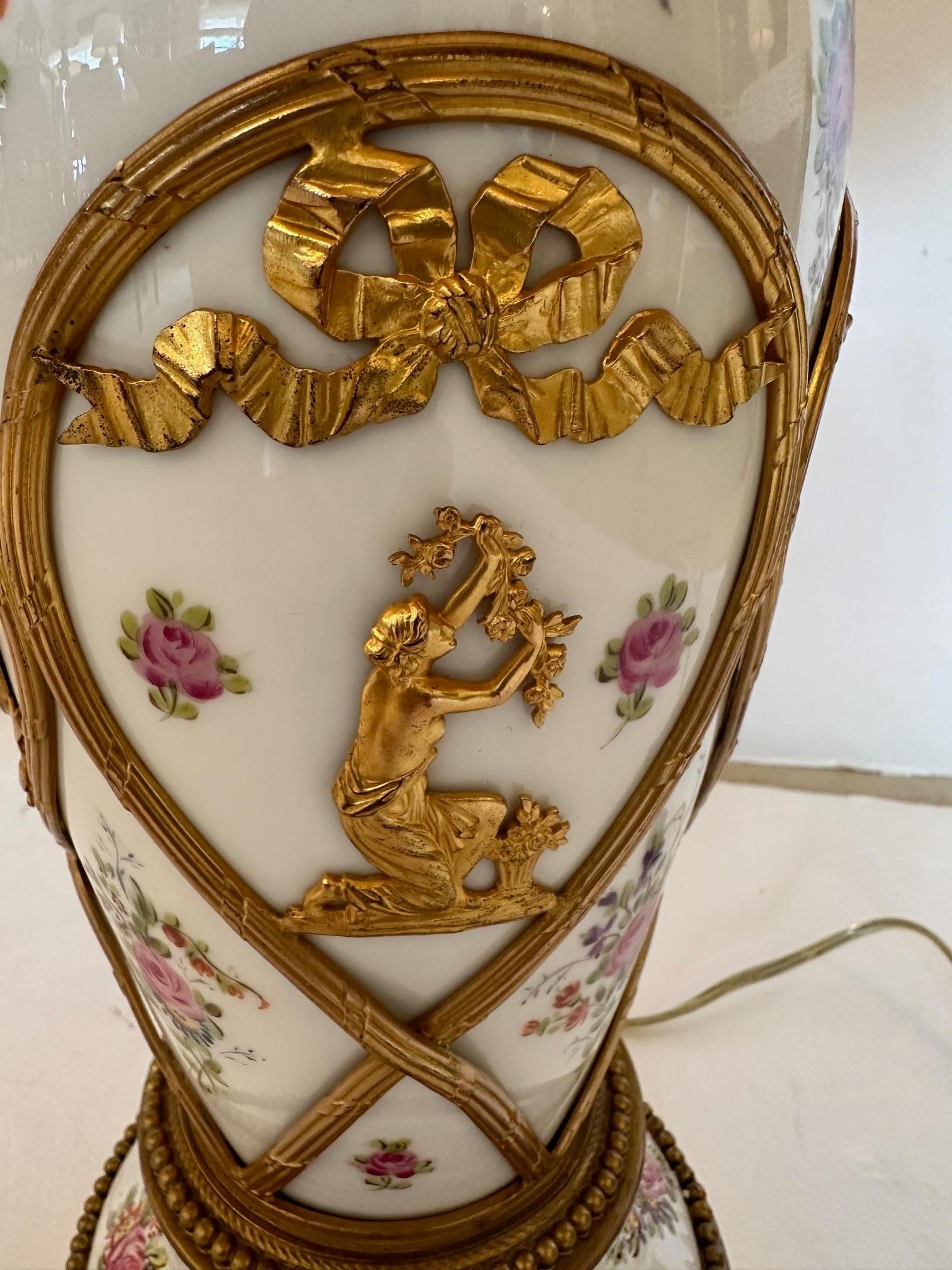 Very pretty pair of white porcelain table lamps having painted pink flowers and green garlands embellished with brass overlay of bows and figures.