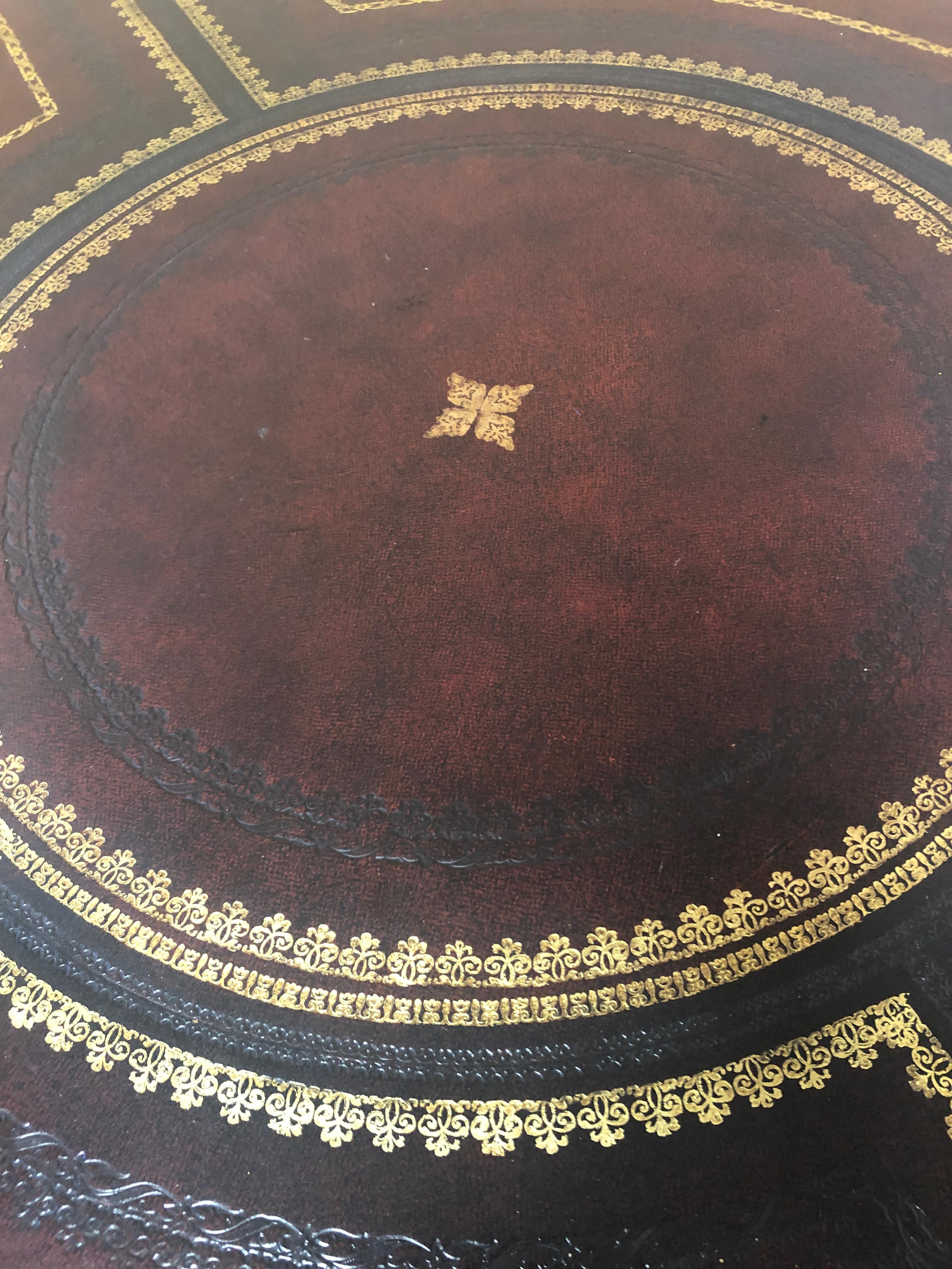 Marvelous round leather wrapped center table having amazing gold tooled decoration everywhere, beautiful brass paw feet on casters, pedestal base with four splayed legs, and 4 drawers around the periphery.