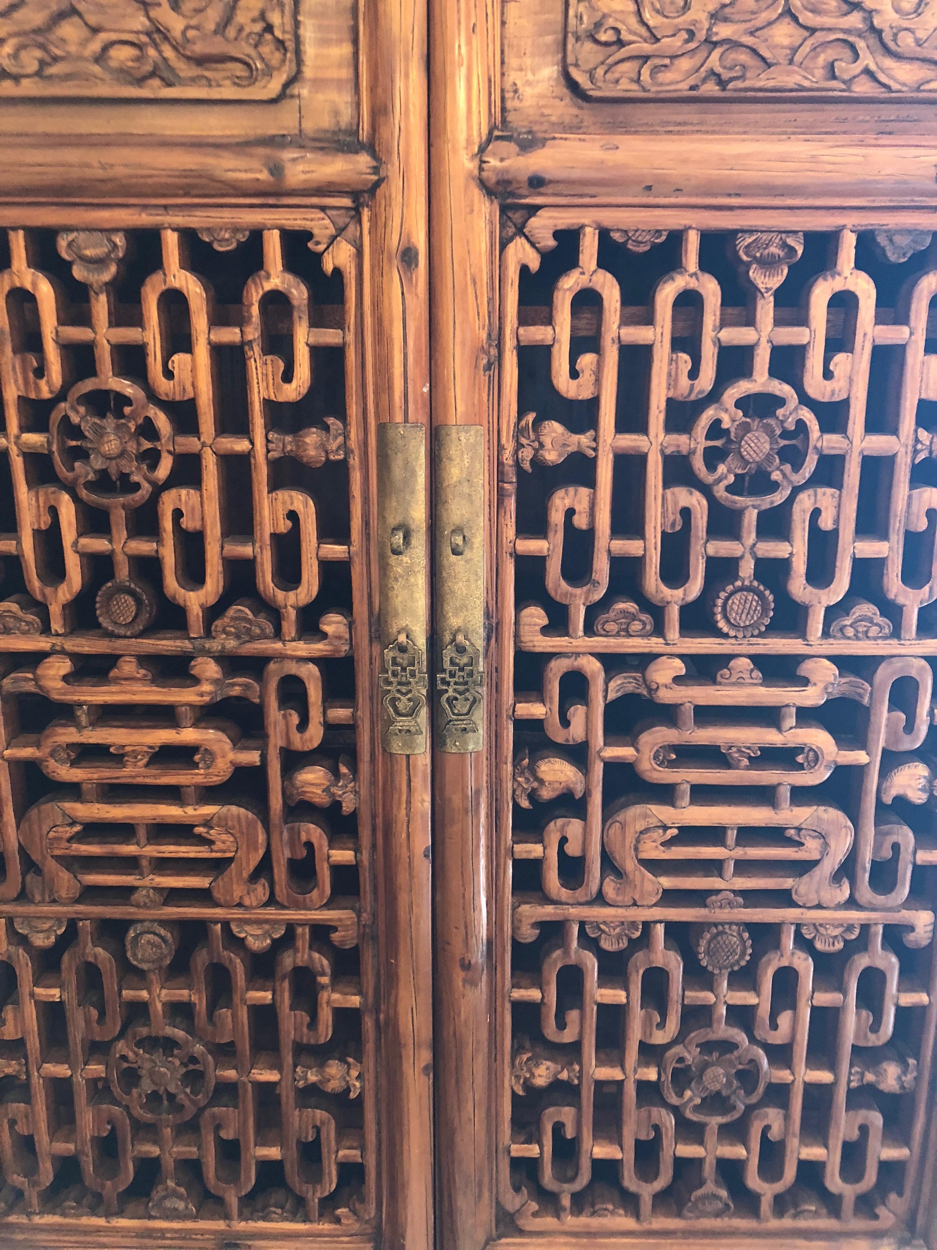 A beautiful and versatile Chinese cabinet in Asian hardwood having latticed and hand-carved doors and two lower drawers. Interior is comprised of 3 shelves which are removable. One shelf is a lighter color, as was replaced. Lovely original brass