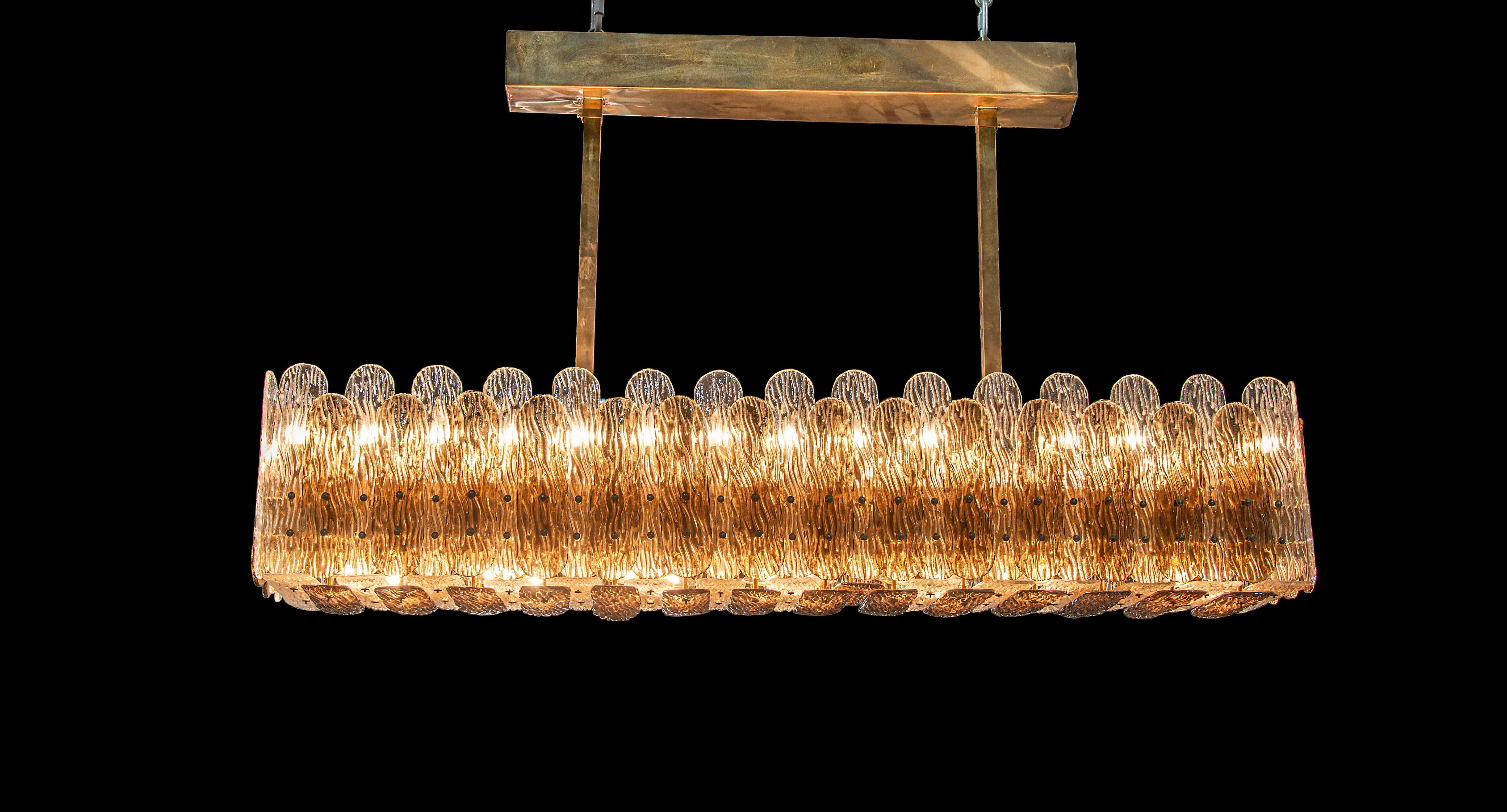 A rectangular frame of polished brass with overlapping panels of shimmering textured clear and smoke glass make for a bold dining feature.

Thomas Cooper Studio represents a multilayered, multifaceted collaboration, where materials and techniques