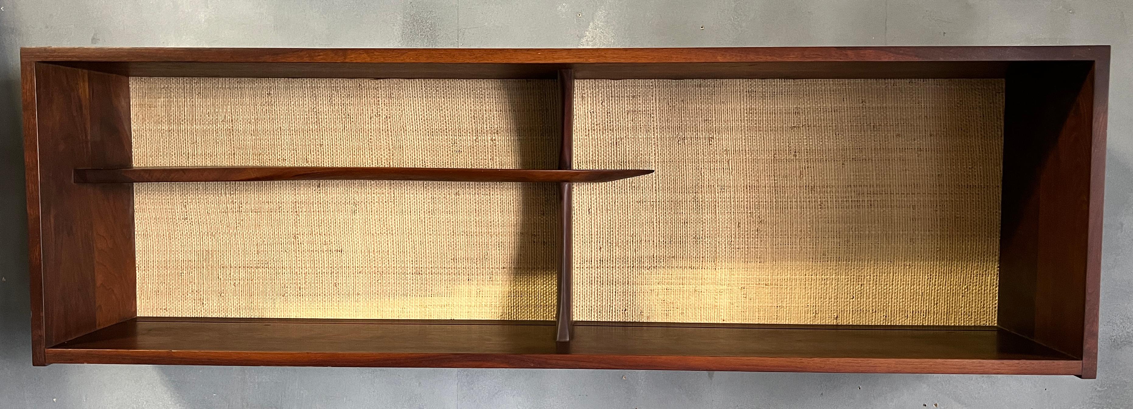Amazing wall mounted shelf hand crafted in black walnut by Phillip Powell. Signature dovetailed edges and choice walnut stand in contrast with the grass cloth backing. Sculptural shelves take up half the case piece. Shelf measures 9.5