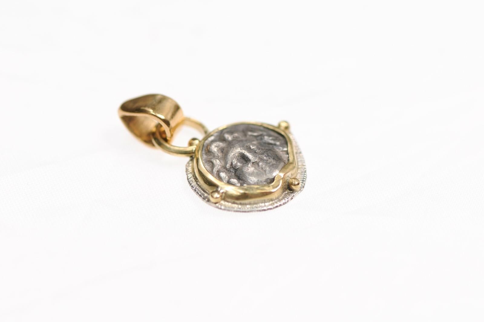 Un ciondolo Obolo AR rivolto verso la Gorgonia e rifinito con oro 22k e argento sterling. L'origine di questo Obolo AR è la Pisidia, Selge, circa 350-300 a.C.. La moneta originale misura 11 mm di diametro e pesa 0,80 grammi. Questo angelico e