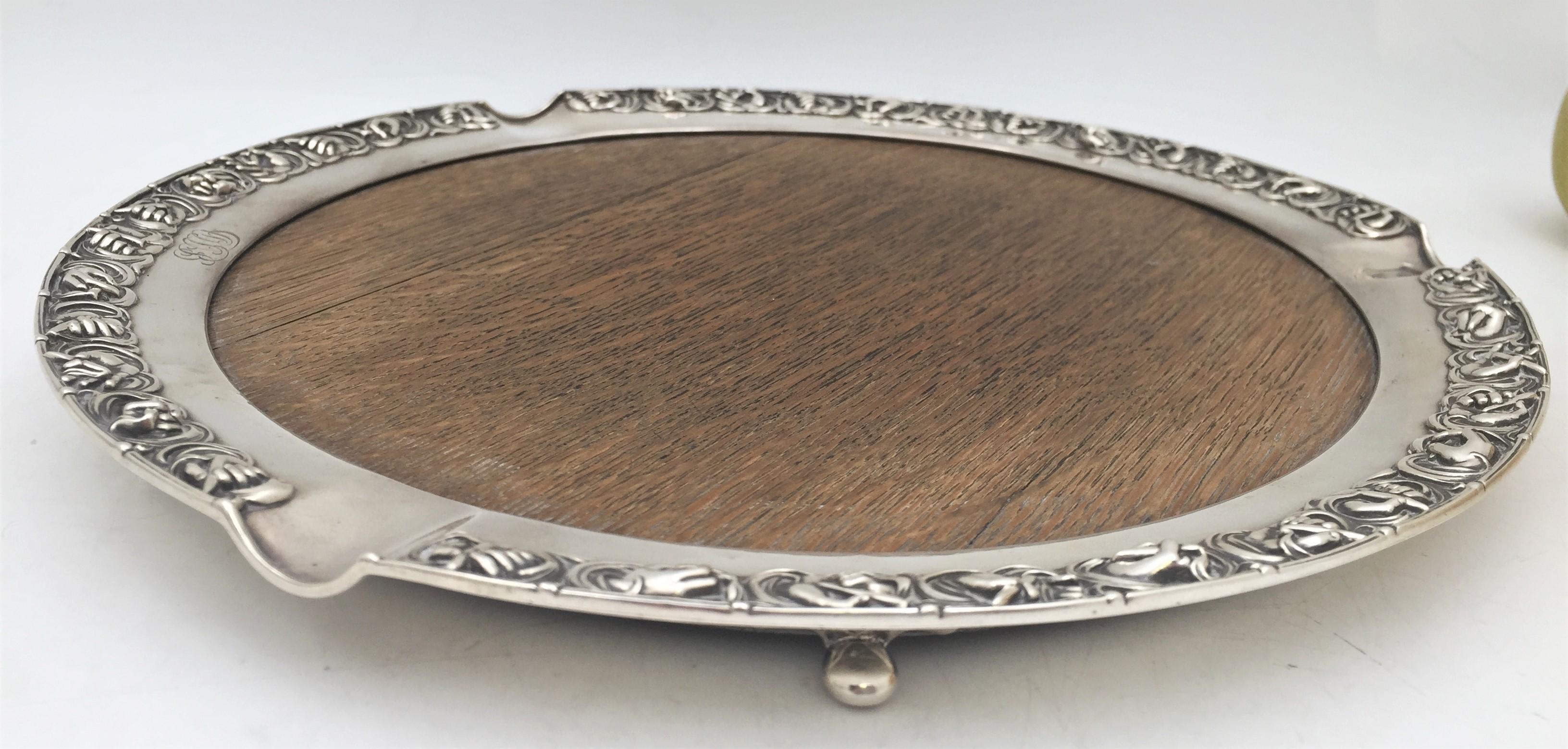 Rare plateau Gorham en argent sterling et bois de chêne de 1917 avec une bordure ornée de motifs de mains en relief reposant sur 4 pieds à billes. Elle mesure 13 1/4'' de diamètre par 1 1/4'' de hauteur et porte les poinçons comme indiqué. 

Au