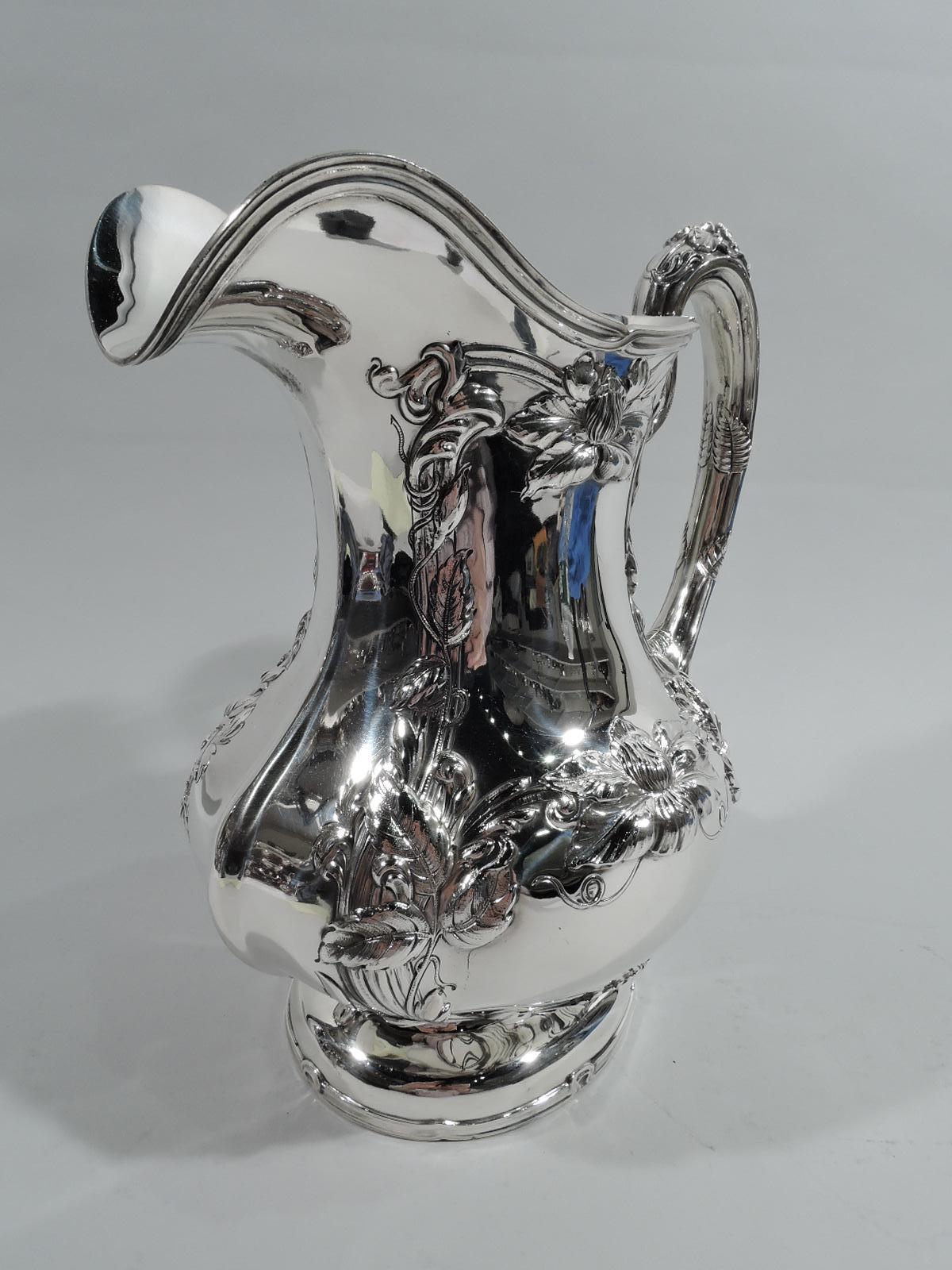 Art Nouveau sterling silver water pitcher. Made by Gorham in Providence in 1910. Ovoid with bellied bowl, helmet mouth, and flower capped and fern-wrapped high-looping handle. Shaped trellis frames entwined with profusion of flowers on front and