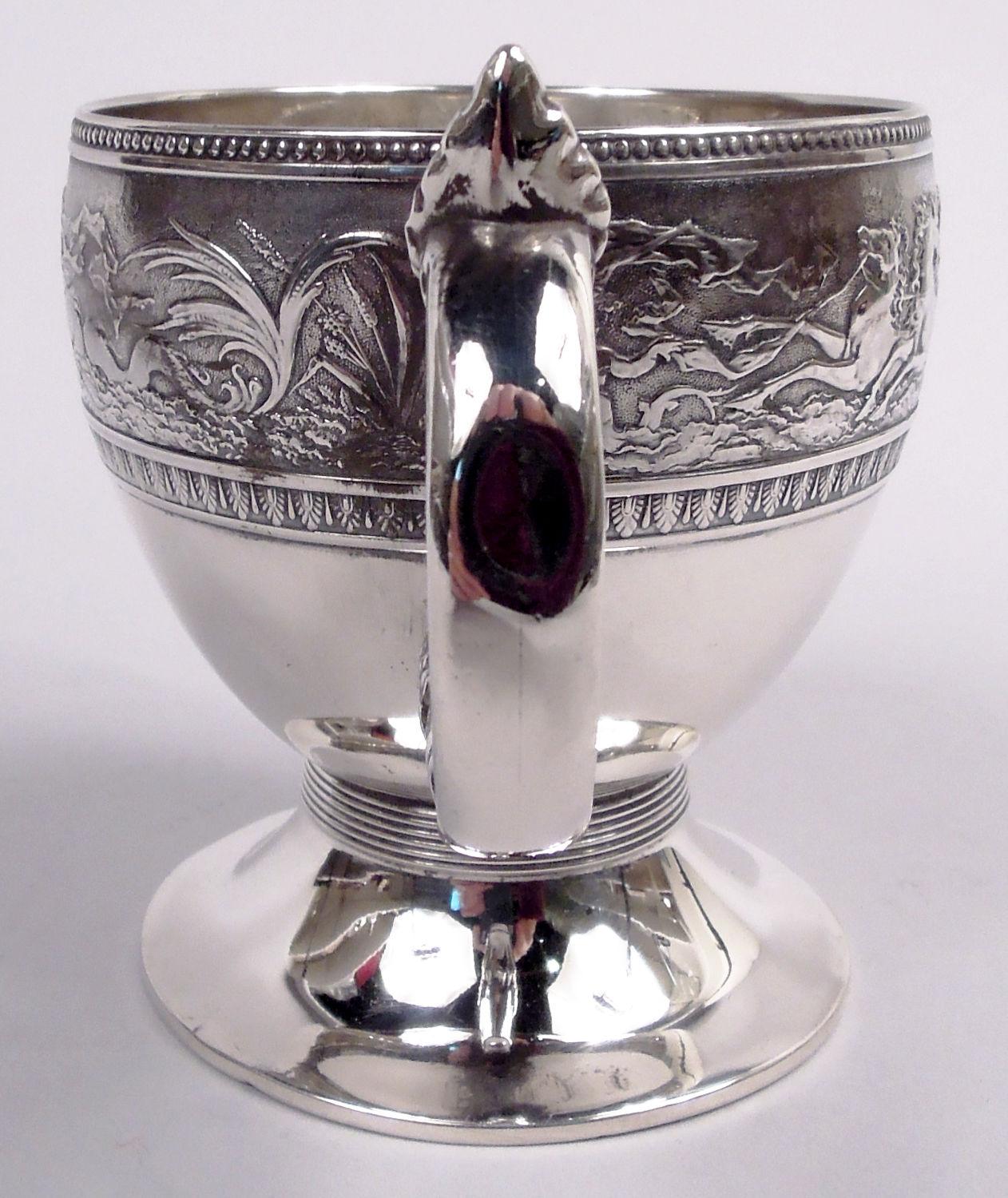 Coppa Aurora in argento sterling per giovani. Prodotto da Gorham a Providence nel 1874. Ciotola tonda e ricurva su piede a listello e allargato; manico ad anello con foglie e ghianda, sempre a listello. Fregio in gesso raffigurante cavalli al
