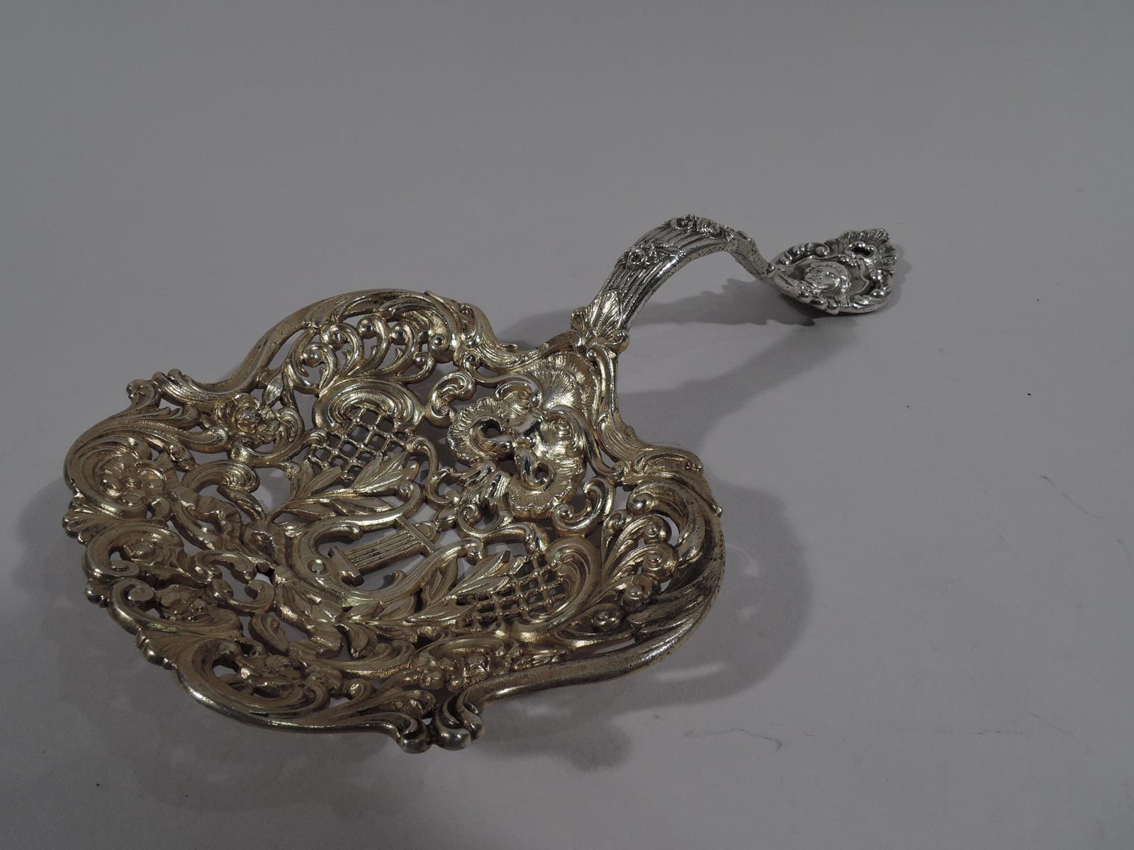 Turn-of-the-century Belle Époque sterling silver bonbon scoop. Made by Gorham in Providence. Shaped and gilt bowl with pierced scrolls, flowers, diaper, and central lyre. S-scroll and reeded handle. Leafy terminal inset with Classical mask. Fully