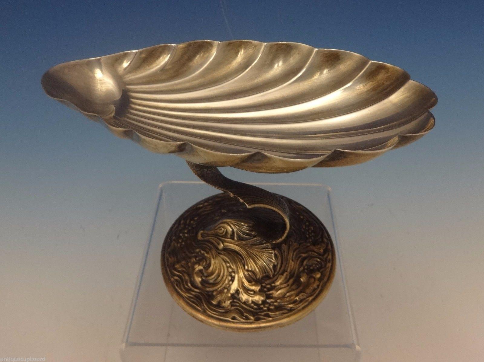 Gorham-Durgin
Gorham-Durgin sterling silver pair of raised compotes marked #107. They feature a seashell bowl atop a dolphin on a water and seaweed base. These pieces measure 4 tall, 5 3/4 long, and have a combined weight of 10.4 ozt. They date