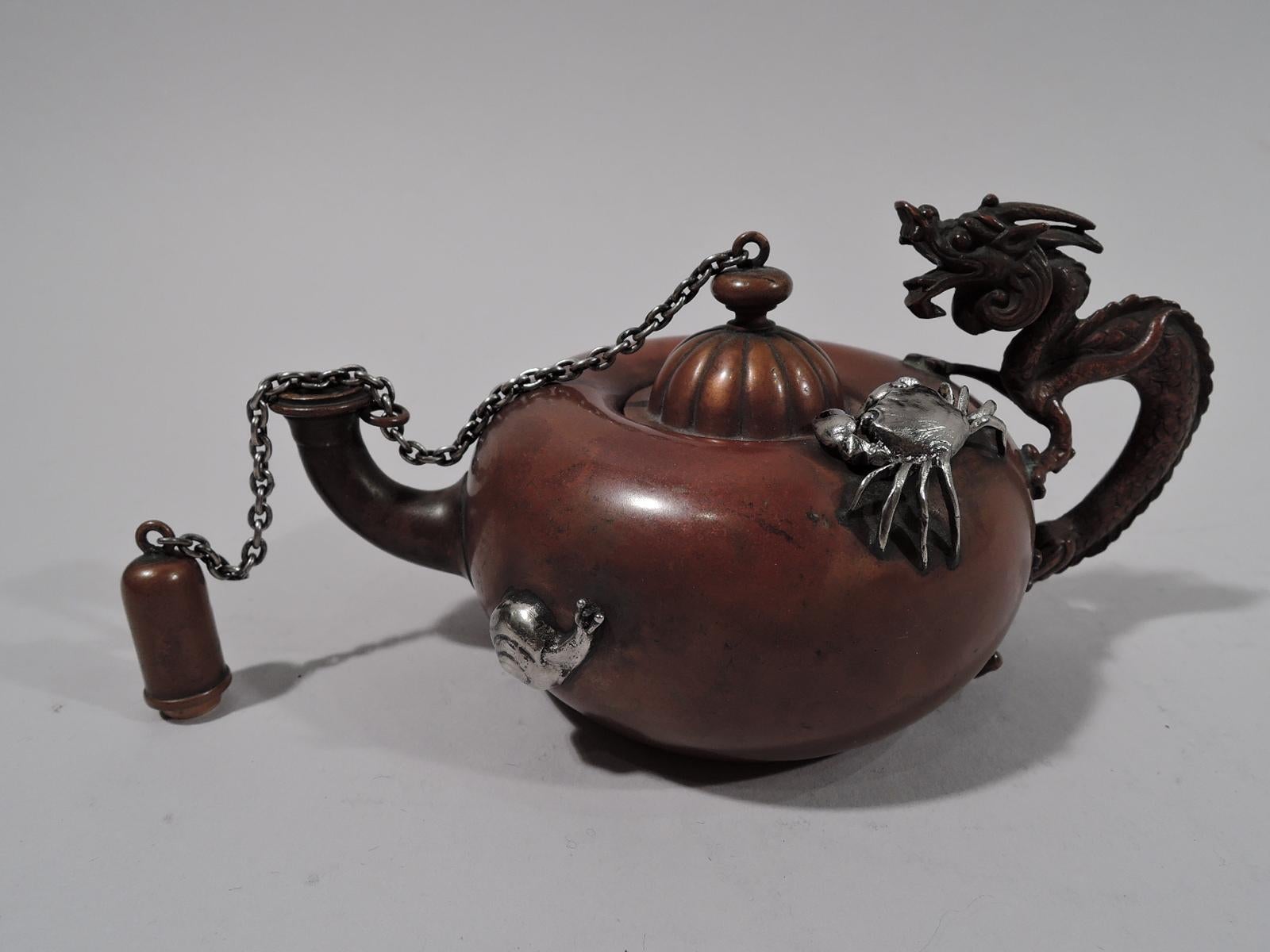 Japonesque mixed metal cigar lighter. Made by Gorham in Providence in 1903. Copper teapot-form with bellied body and cast handle in form of dragon, horned head and talons gripping sides. Upturned spout with chained cap. Also chained is domed and