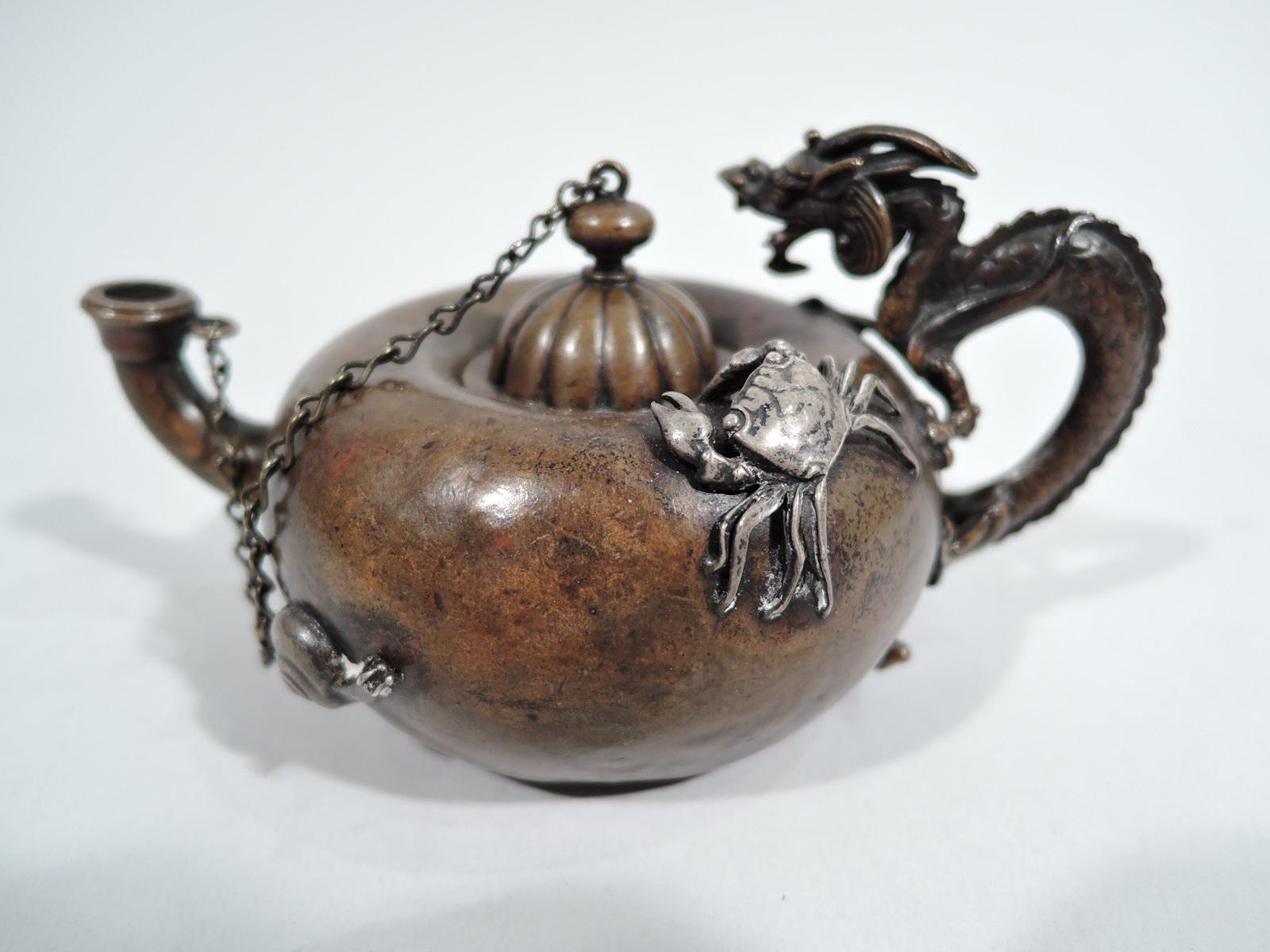 Japonesque mixed metal cigar lighter. Made by Gorham in Providence in 1905. Copper saki-pot form with bellied body and cast handle in form of dragon with horned head and talons gripping sides. Upturned spout. Domed and lobed cover chained to spout.