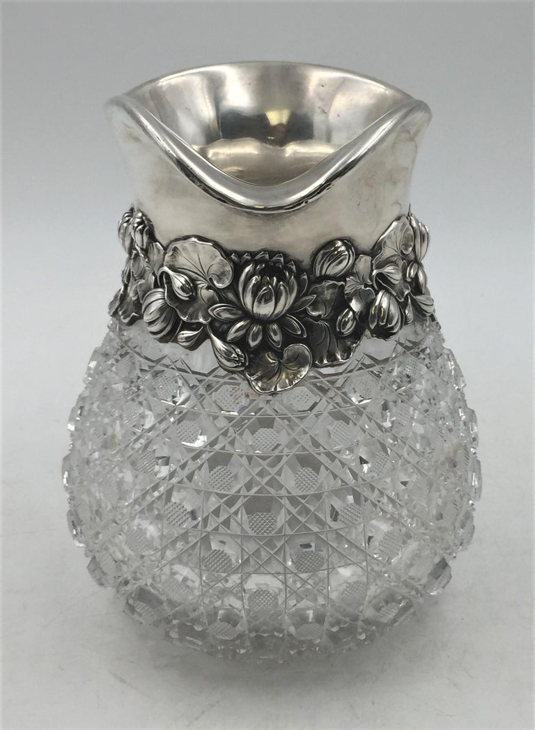 Early 20th century, Gorham sterling silver and cut glass pitcher or vase in Art Nouveau style with applied, dimensional peonies and stylized leaves around the body. It measures 8'' in height by 8 1/4'' from handle to spout approximately by 6 1/2''