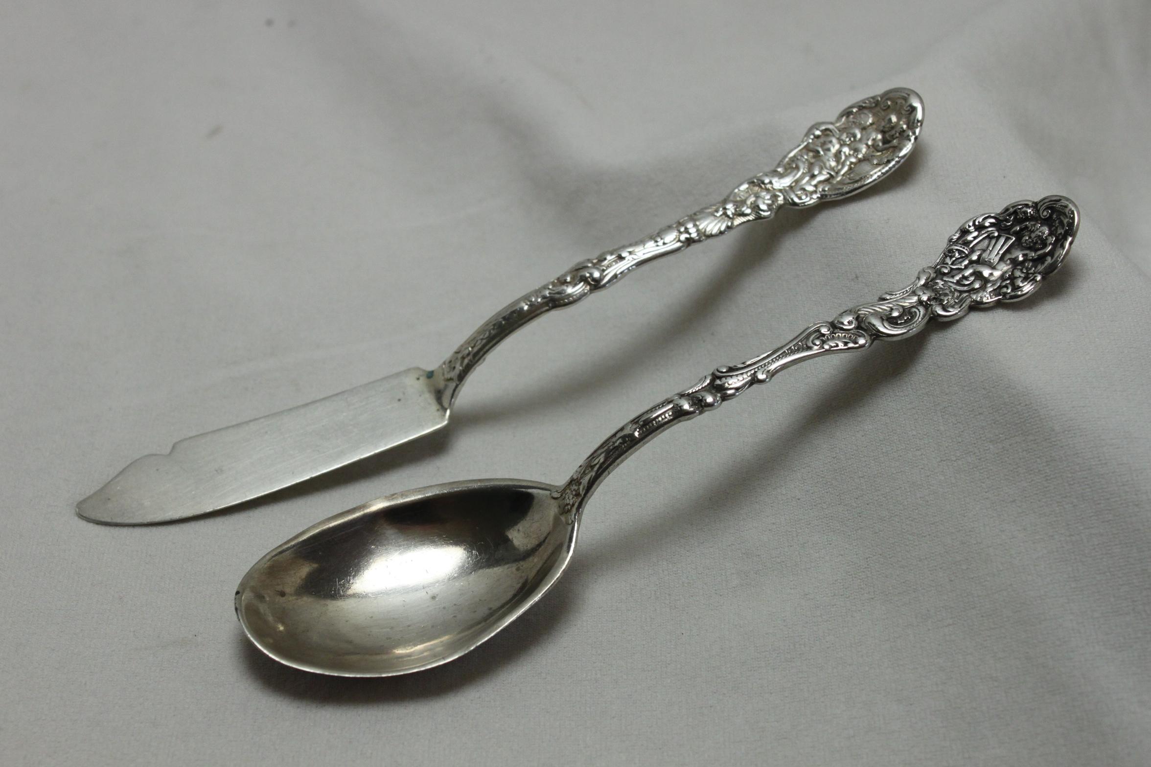 These two pieces of Gorham sterling silver flatware are decorated with the Versailles pattern, which was introduced in 1888. The butter knife, or possibly a pickle knife, is 165 mm (6.5 inches) in length and weighs 34 gms. The spoon measures 153 mm