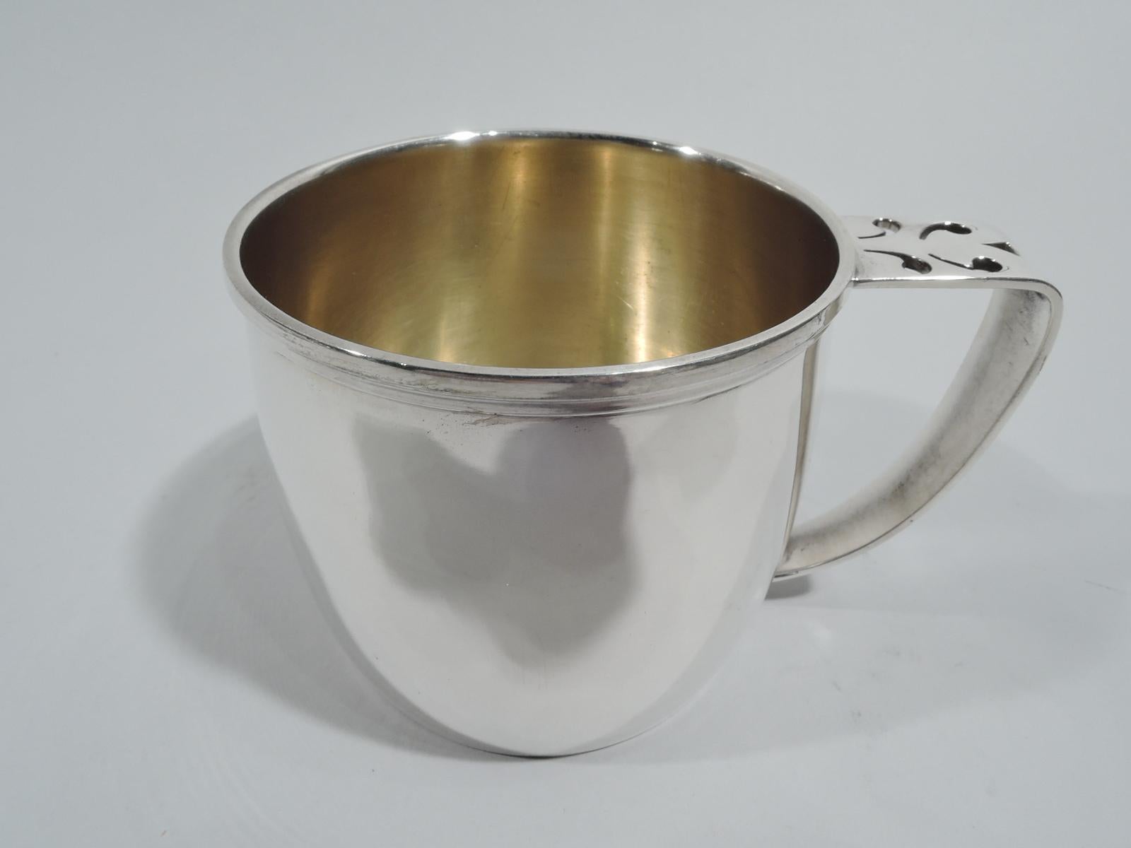 Craftsman sterling silver baby cup. Made by Gorham in Providence, ca 1920. Gently curved sides and molded rim. Scroll-bracket handle with pierced ornament. Gilt-washed interior. Sturdy proportions with plenty of room for engraving. Fully marked