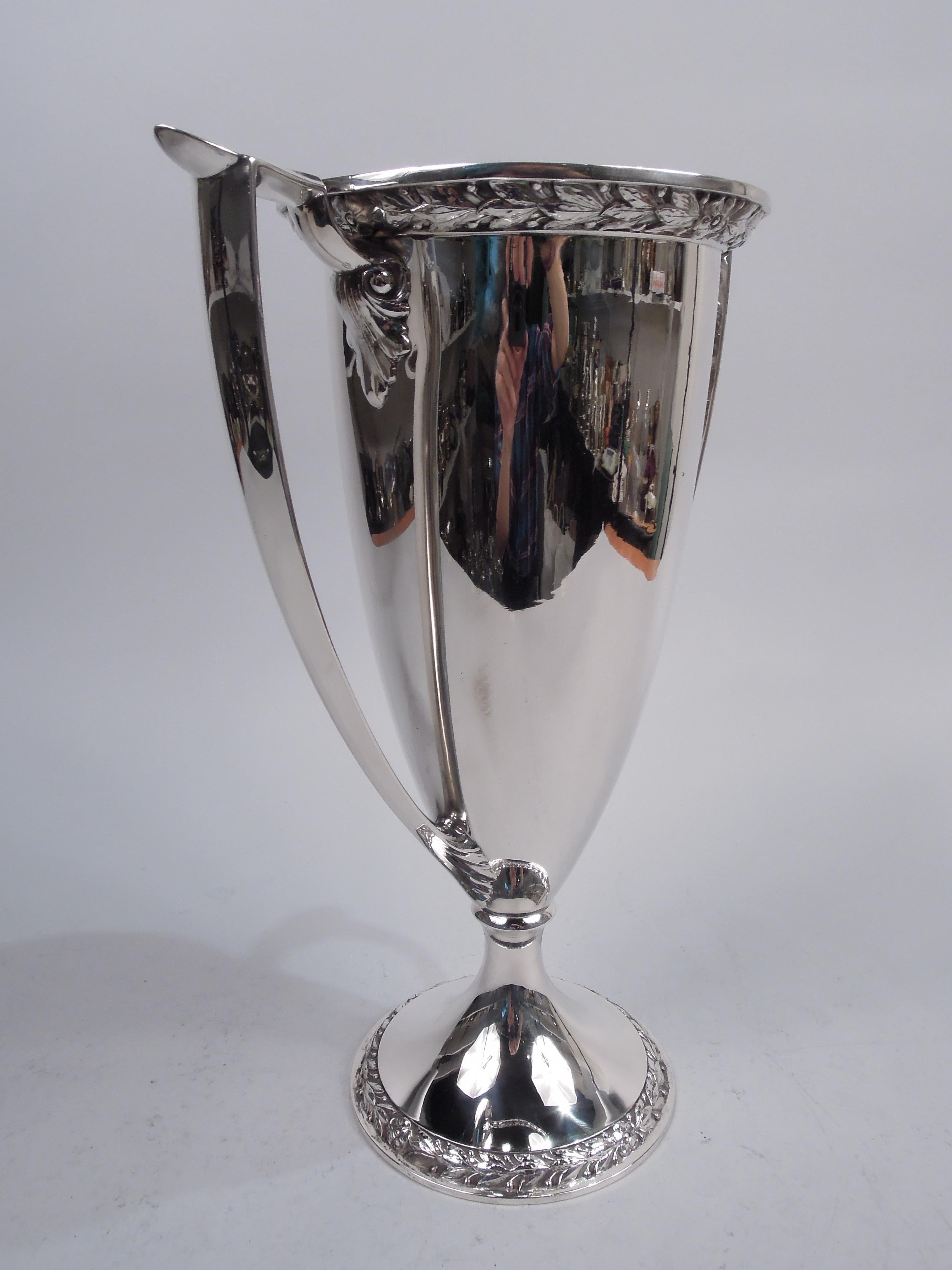 Edwardian Classical sterling silver trophy cup. Made by Gorham in Providence, ca 1910. Tall and tapering bowl with flat mouth rim on domed foot. Capped and leaf-mounted scroll-bracket side handles. Imbricated leaf and flower border applied to mouth