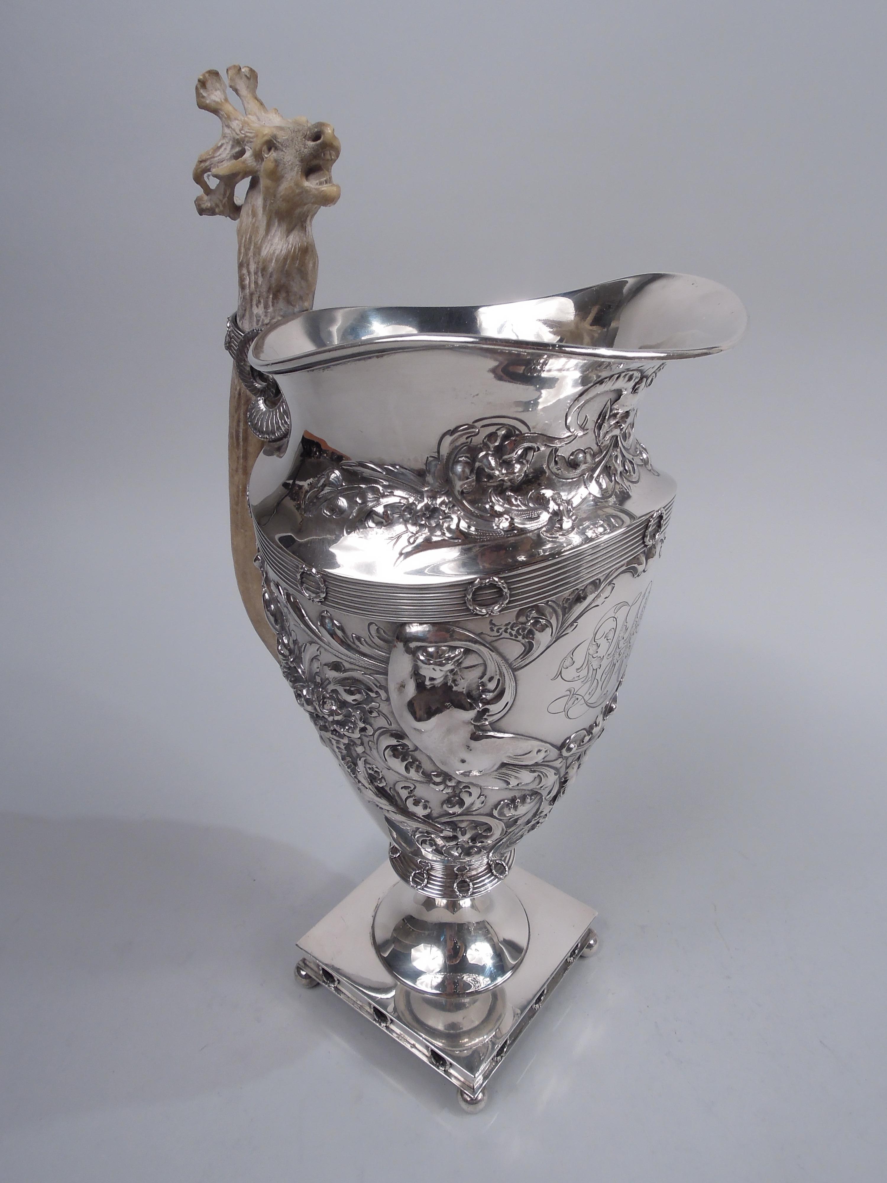 Victorian sterling silver ewer. Made by Gorham in Providence in 1897. Ovoid bowl with helmet mouth and base knop on raised foot mounted to square base on corner ball supports. Chased ornament in form of leafing scrollwork and flowers; two languid