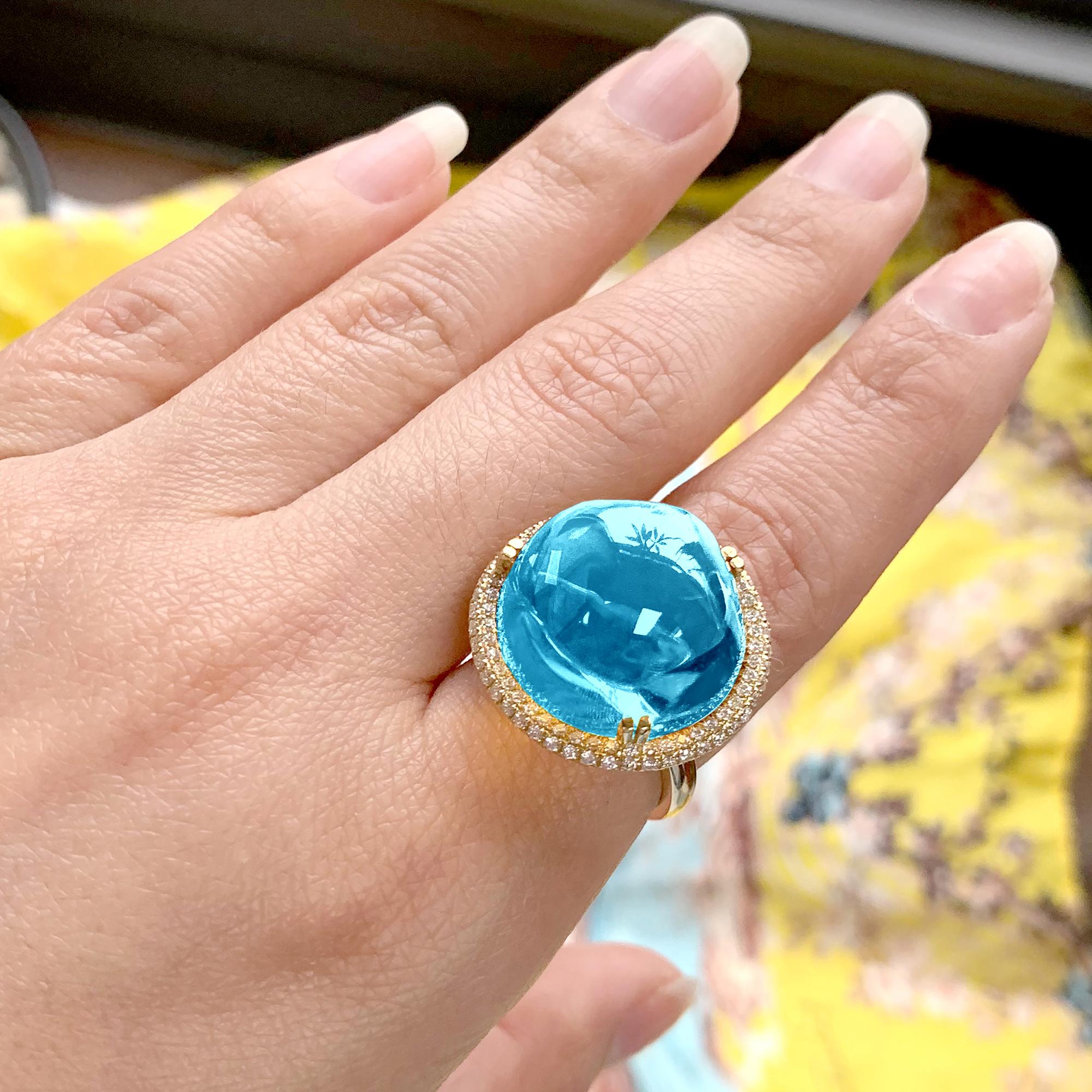 This Blue Topaz Uneven Round Cabochon Ring in 18K Yellow Gold with Diamonds is a stunning piece of jewelry from the 'Rock 'N Roll' Collection. The ring features a beautiful, unevenly-shaped round cabochon blue topaz, set in a sleek 18K yellow gold