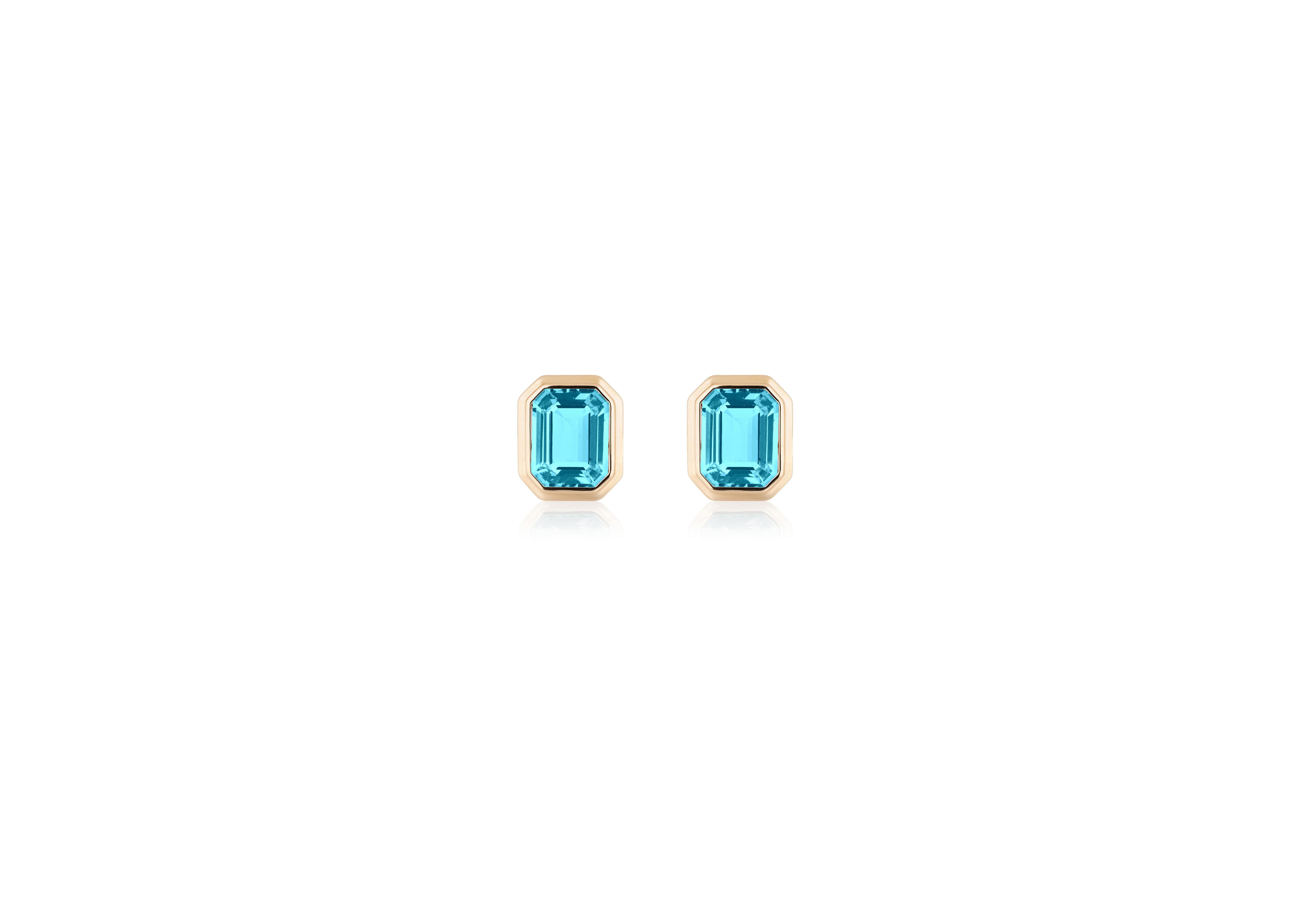These Blue Topaz Emerald Cut Bezel Set Stud Earrings in 18K Yellow Gold from the 'Manhattan' Collection are an exquisite pair of earrings that exude elegance and sophistication. These earrings feature vibrant blue topaz gemstones with a captivating