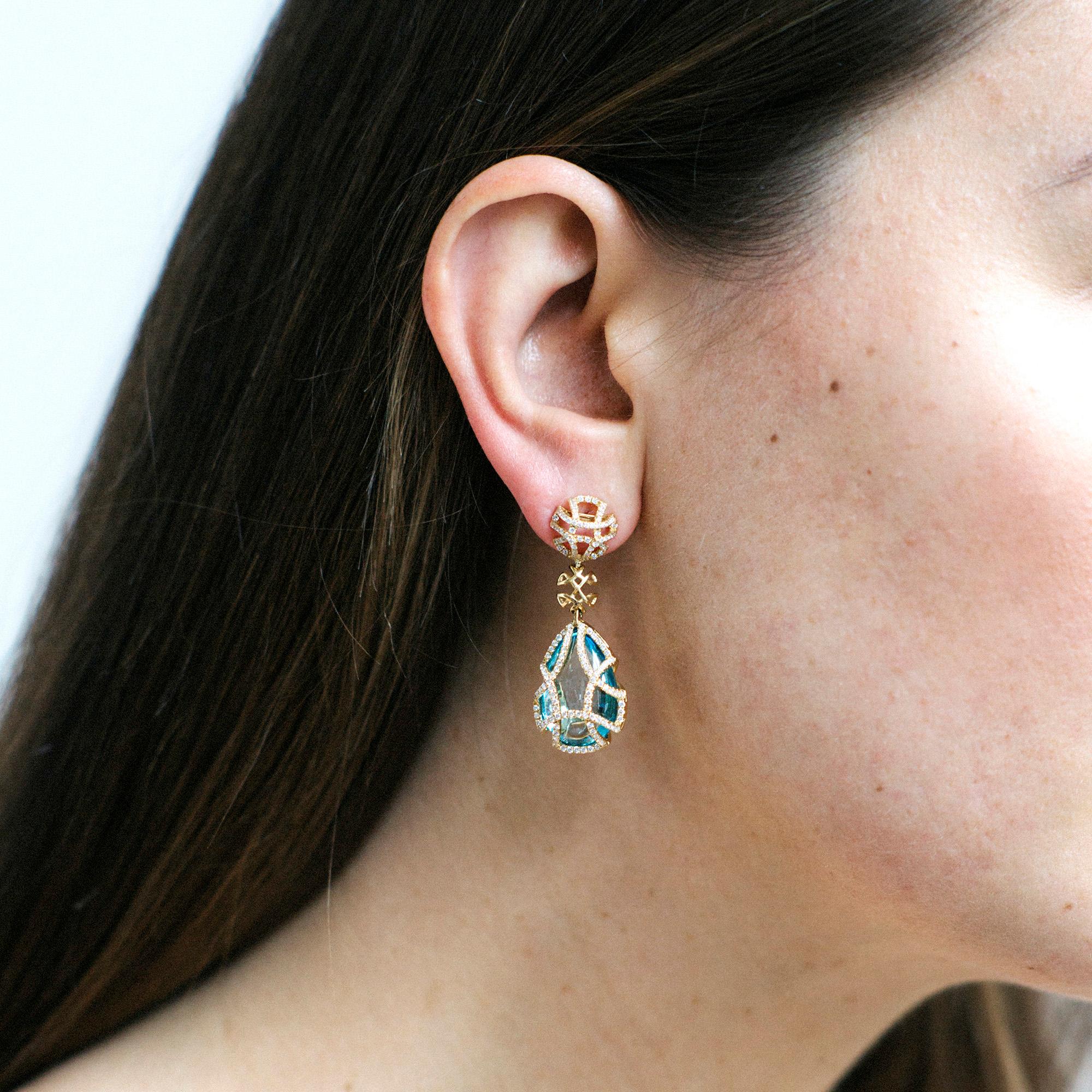These Blue Topaz Teardrop Cage Earring with Diamonds in 18K Yellow Gold is a stunning piece of jewelry from the 'Freedom' collection. The earring features a teardrop-shaped blue topaz gemstone set in a delicate cage-like structure made of 18K yellow