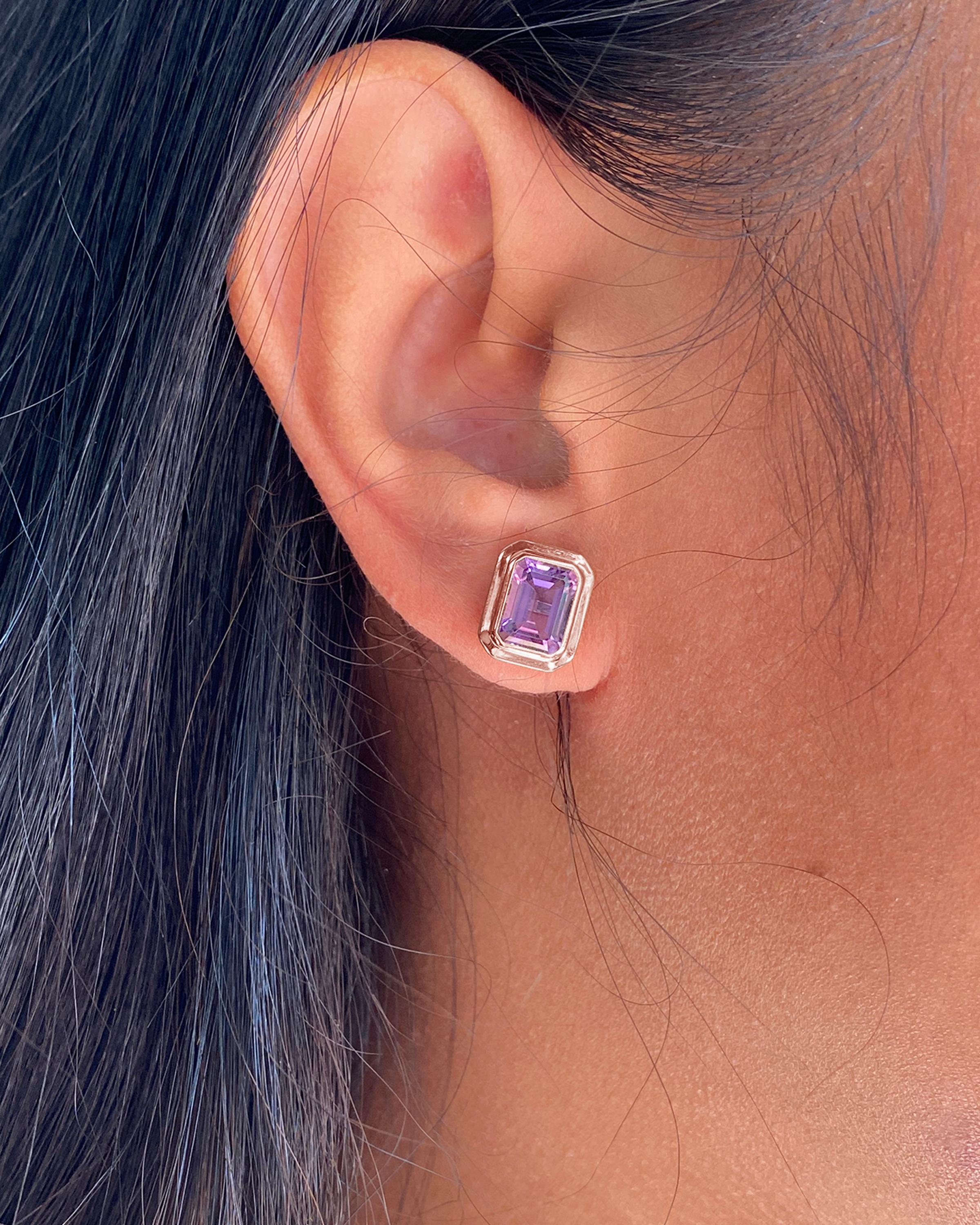 The Lavender Amethyst Emerald Cut Bezel Set Stud Earrings in 18K Rose Gold are exquisite pieces from the 'Manhattan' Collection. These stunning earrings feature a pair of vibrant lavender amethyst gemstones, each expertly cut in an elegant emerald
