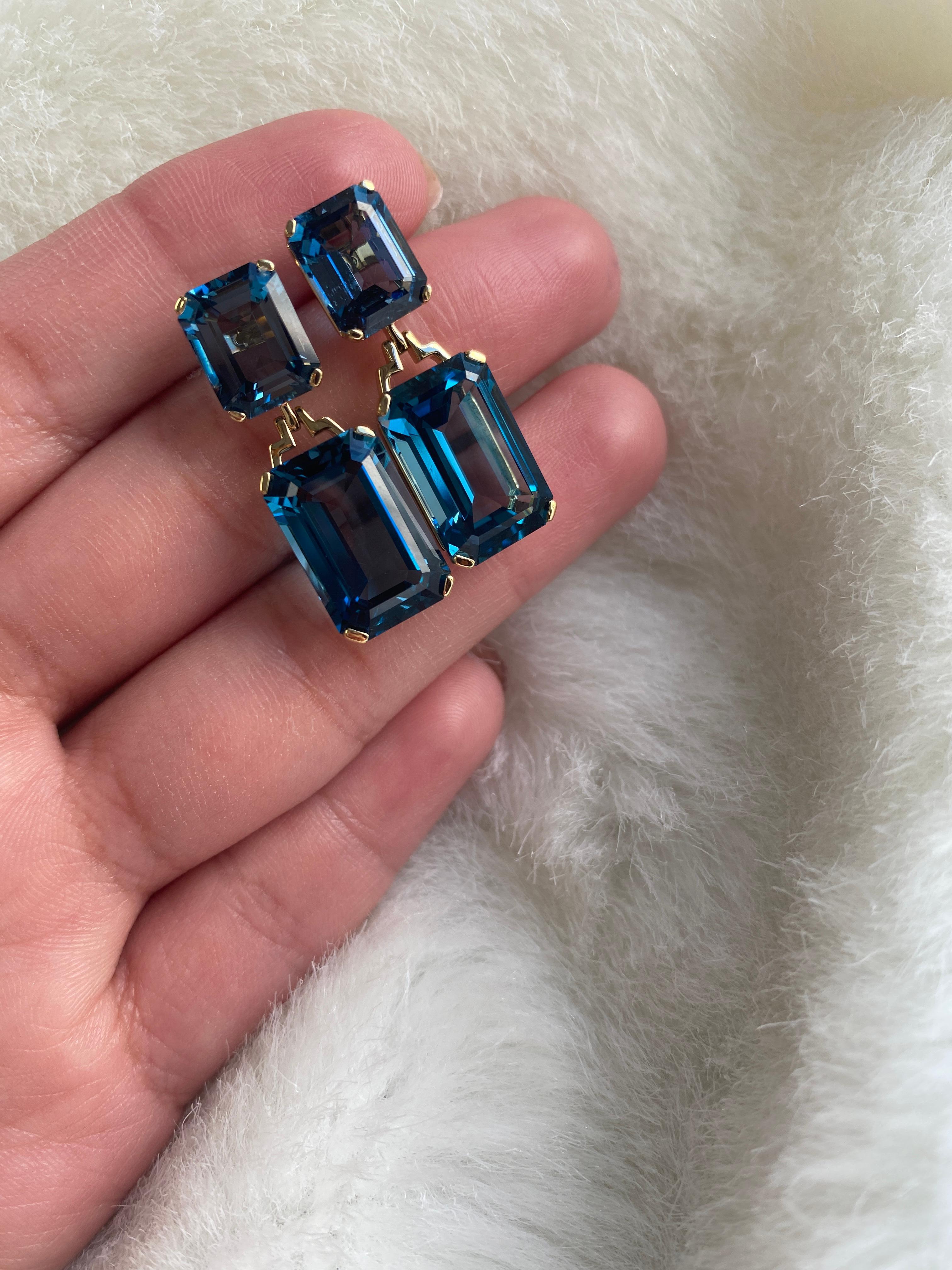 These London Blue Topaz Emerald Cut Earrings in 18K Yellow Gold from the 'Gossip' Collection are a stunning and sophisticated accessory. The deep blue hue of the London blue topaz stones, combined with the elegant emerald cut design, creates a