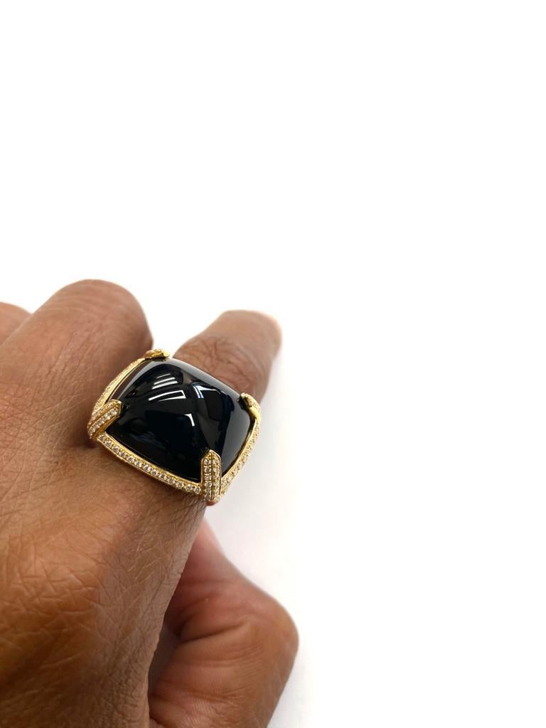 The Onyx East-west Cabochon Ring with Diamonds in 18k Yellow Gold is a stunning piece of jewelry from the 'Rock N Roll' collection. The ring features a large, sugarloaf onyx set in a horizontal or 