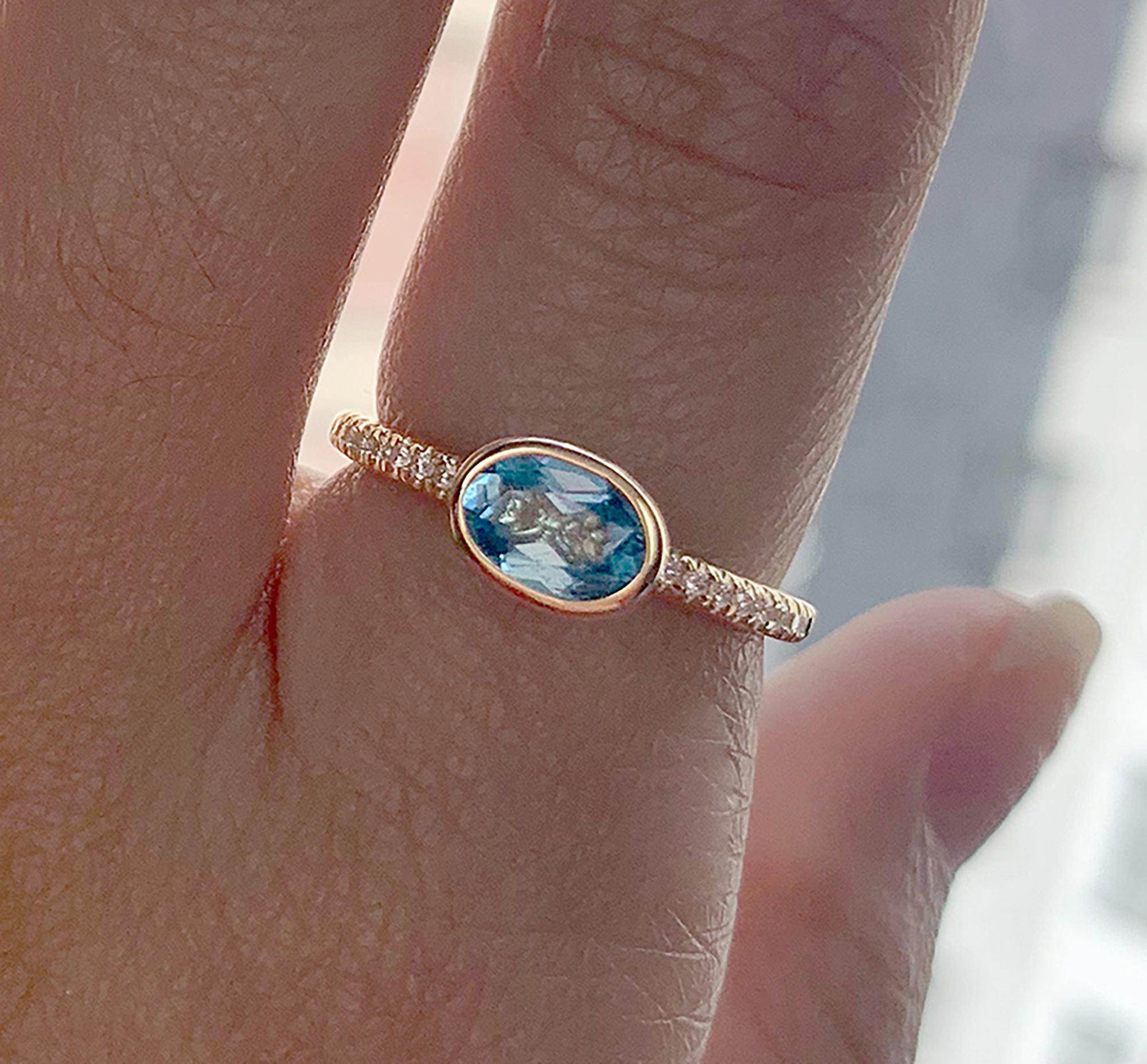 The Blue Topaz Faceted Oval Stackable Ring with Diamonds in 18K Yellow Gold is a stunning piece of jewelry from the 'Gossip' Collection. The ring features a beautiful blue topaz stone in an oval shape, with a faceted cut that catches the light and