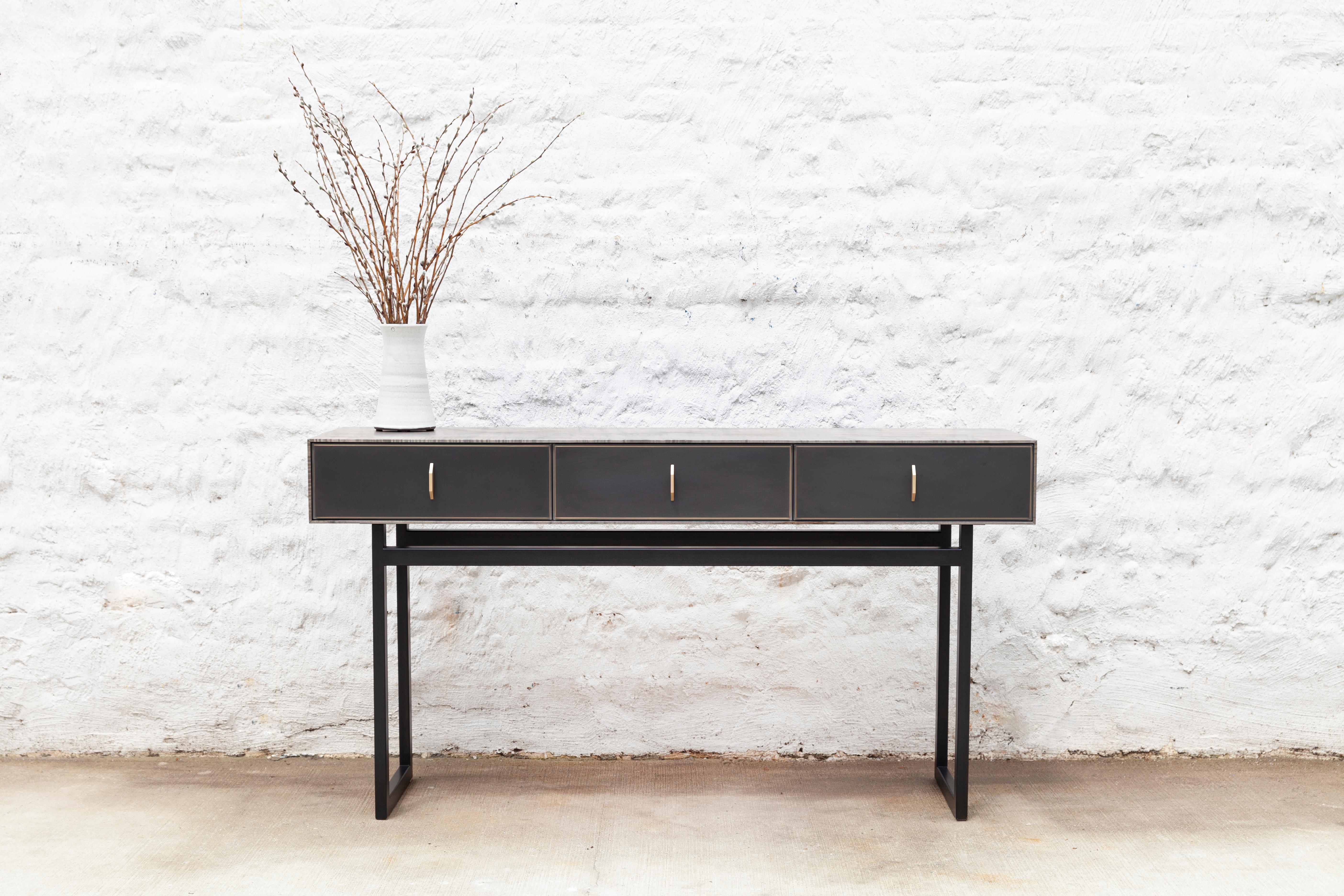 The harmonious mix of materials enhances the beauty of this Gotham console. The console features rich oxidized Ambrosia maple wood, a blackened steel frame, three blackened bronze encased in epoxy resin drawers with black leather lining and