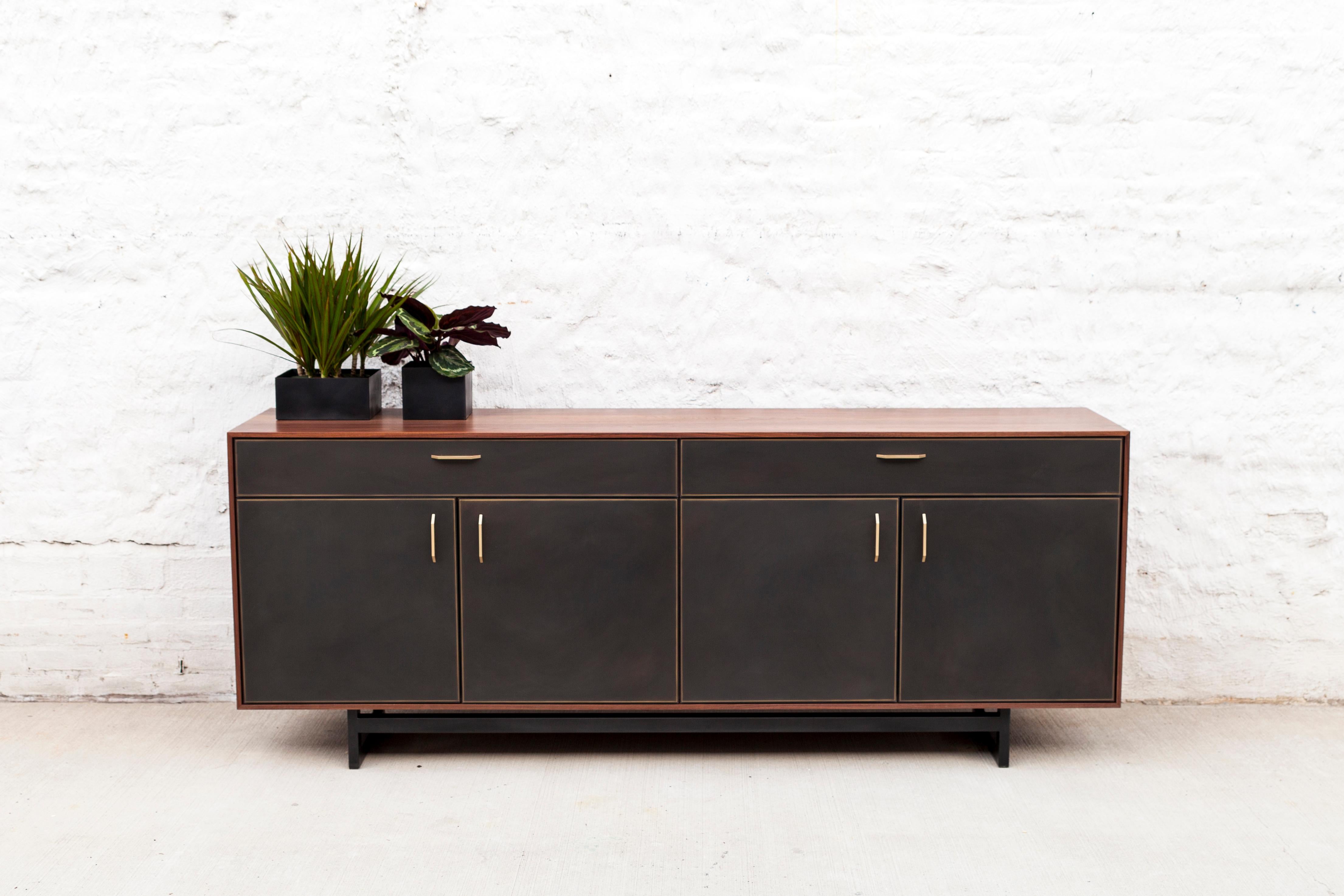 The Gotham credenza features clean lines that blend harmoniously with the beautiful mix of materials. A walnut frame sits on a blackened steel base. Custom hand-sculpted bronze pulls compliment the striking blackened bronze encased in resin drawer