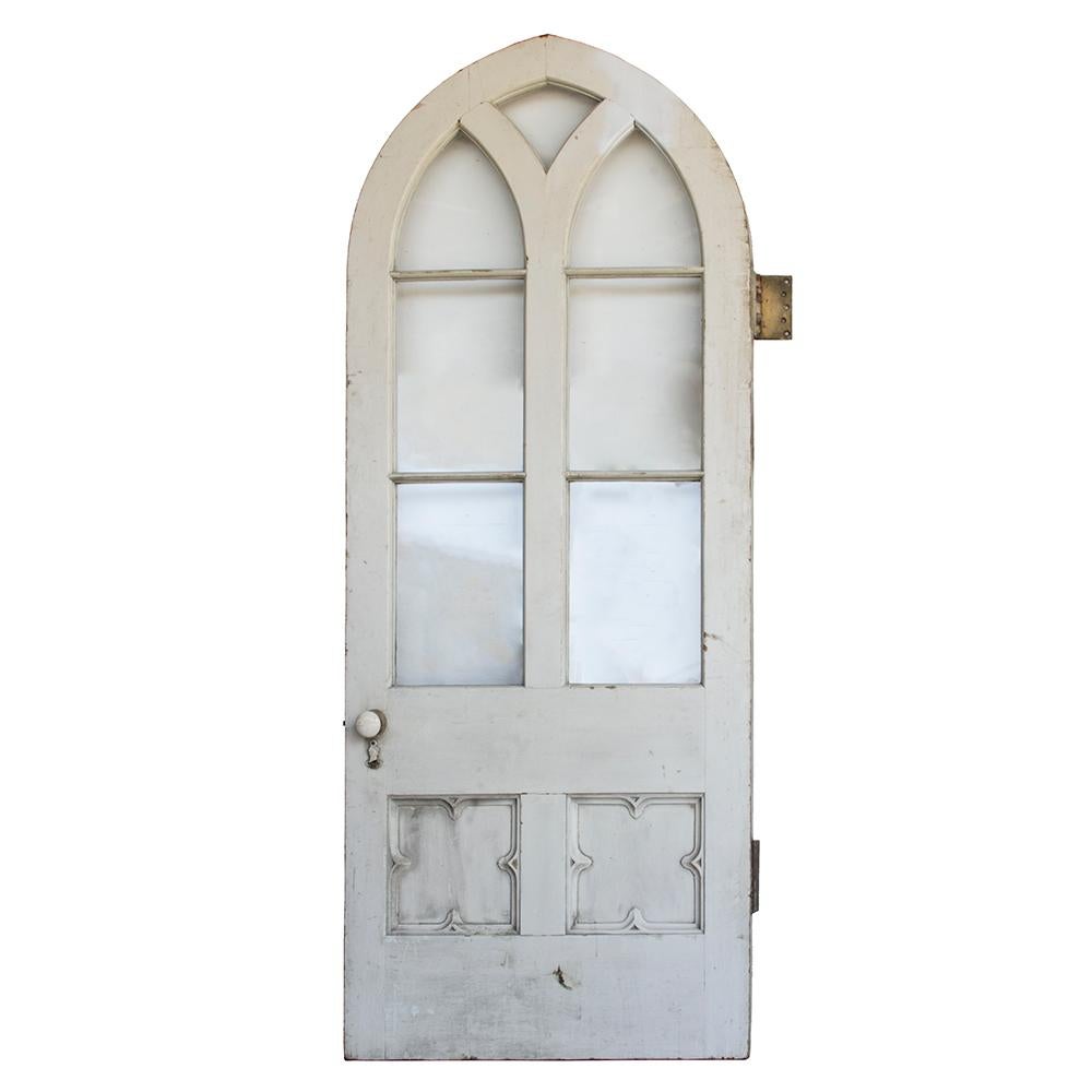 A beautiful and hefty early 2oth century solid wood and glass door, this arched beauty is truly unique. The quatrefoil shaped recessed lower panels have a wonderful Tudor revival appeal and the arched top of the door has been angled to fit into a
