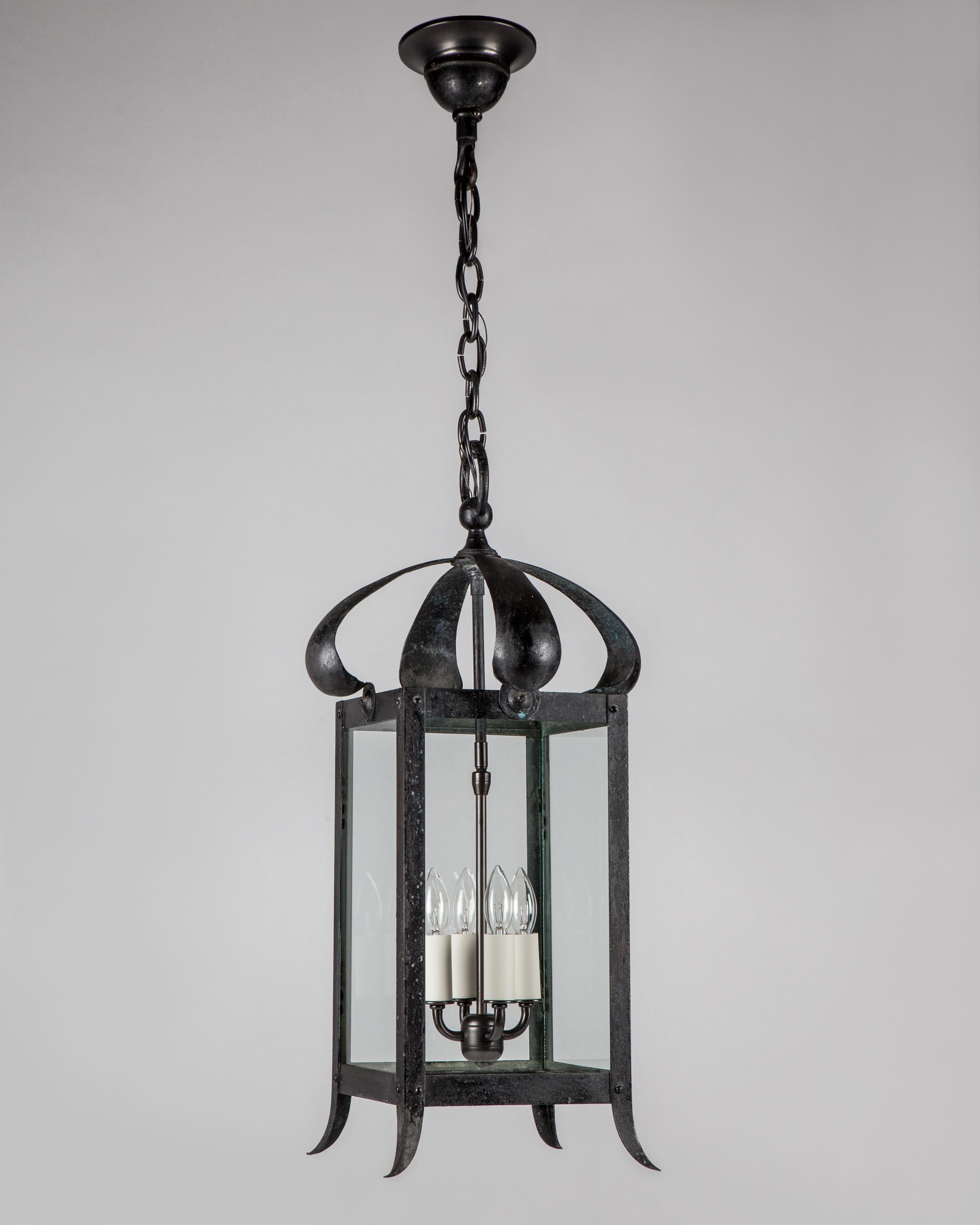 AHL4088
A four sided wrought brass lantern with scroll petal brackets, glazed with clear glass panels, in its original age-blackened patina. Due to the antique nature of this fixture, there may be some nicks or imperfections in the glass. Circa