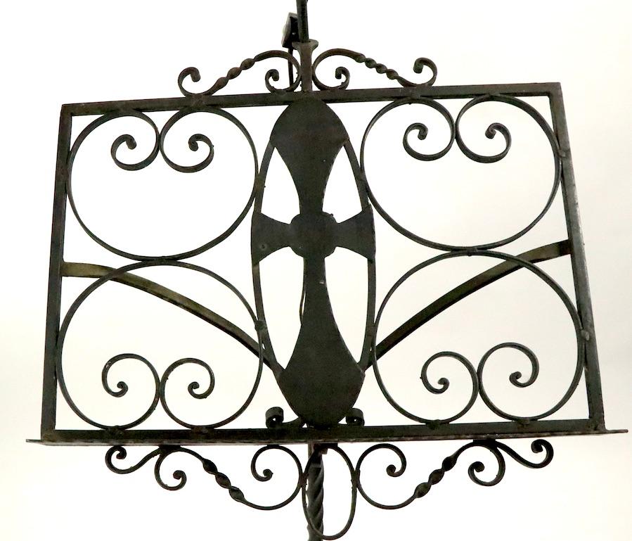 Wrought iron lecturn having an open work book rest with a Gothic cross, and an adjustable hooded light. The hood shade cane be raised or lowered and the bell form shade (11.25 in. diameter) can be tilted back and forth to position and direct the