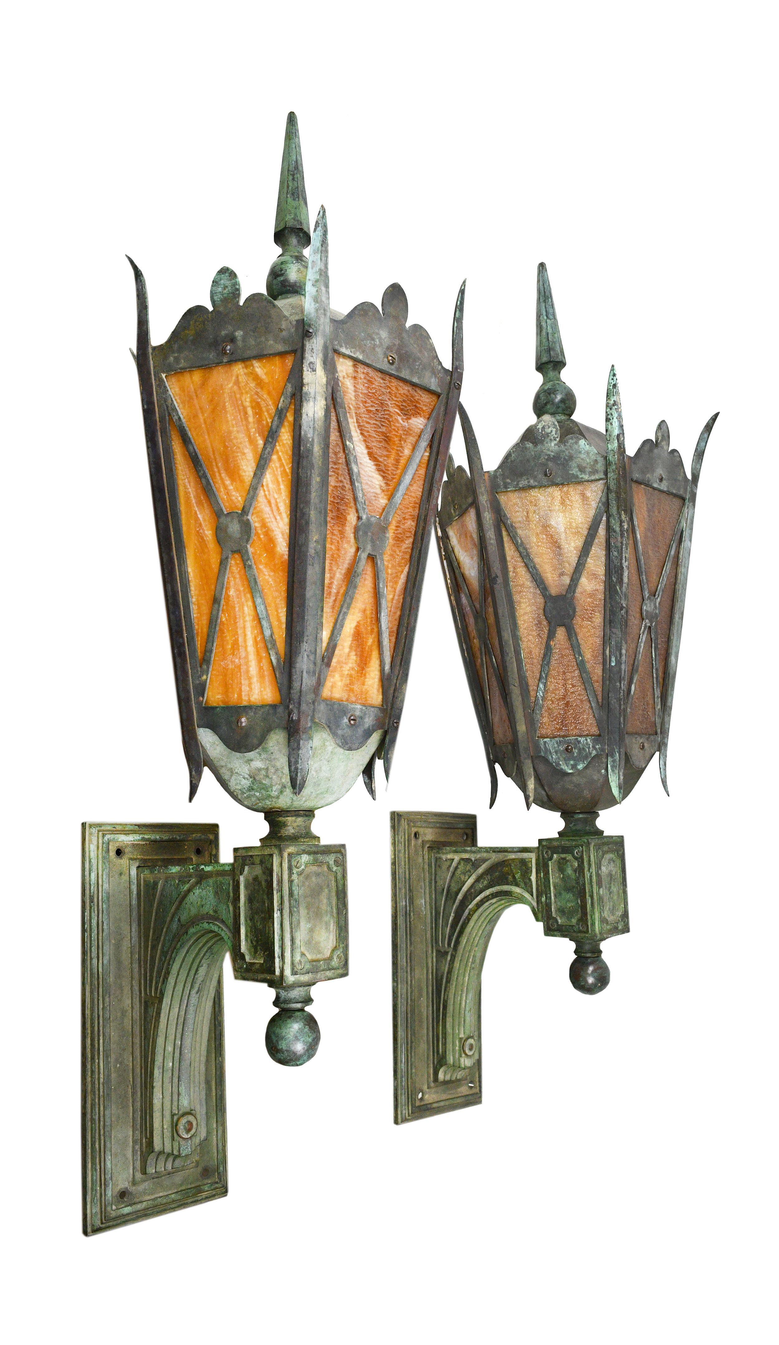 This magnificent pair of exterior sconces with beautiful verdigris patina features a simple lines, curving or angled in all parts except for the connecting elements of the back plate and arm to lantern. Six panes of lovely caramel slag glass give