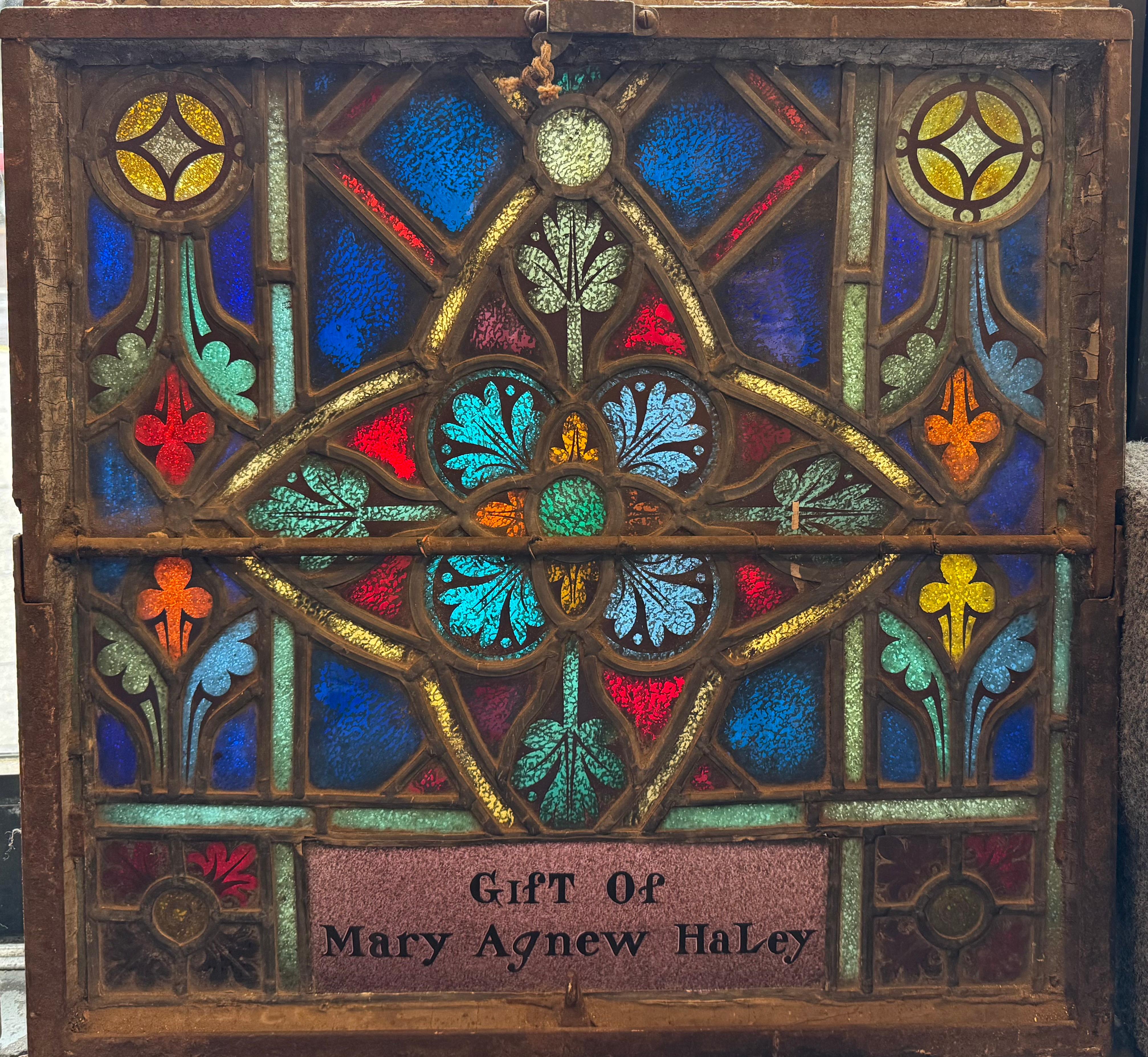 Pair of Gothic style church windows with dedications. Gorgeous stained glass coloring and designs with dedication marker on each. The windows are housed in an iron frame with clear glass outer shield on each. Both windows tilt open. These were