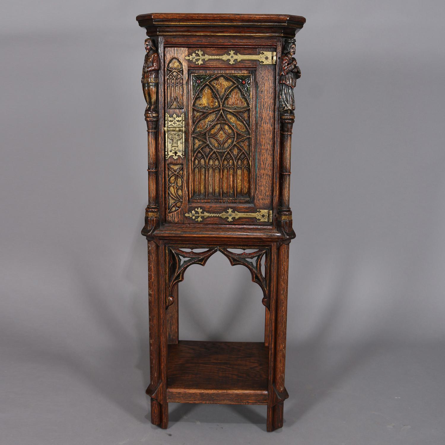 Antique Gothic carved oak cellarette cabinet features polychromed and carved geometric arched decoration with figural guardsmen on corners with single door opening to shelved interior over legs with pierced corbels and lower display shelf, circa