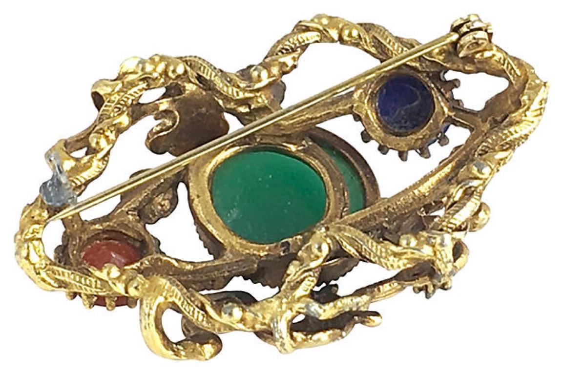 Gothic-style goldtone brooch featuring a double dragon design set with stones made to look like carnelian, green onyx, pearl, and lapis lazuli. Age wear, replacement 