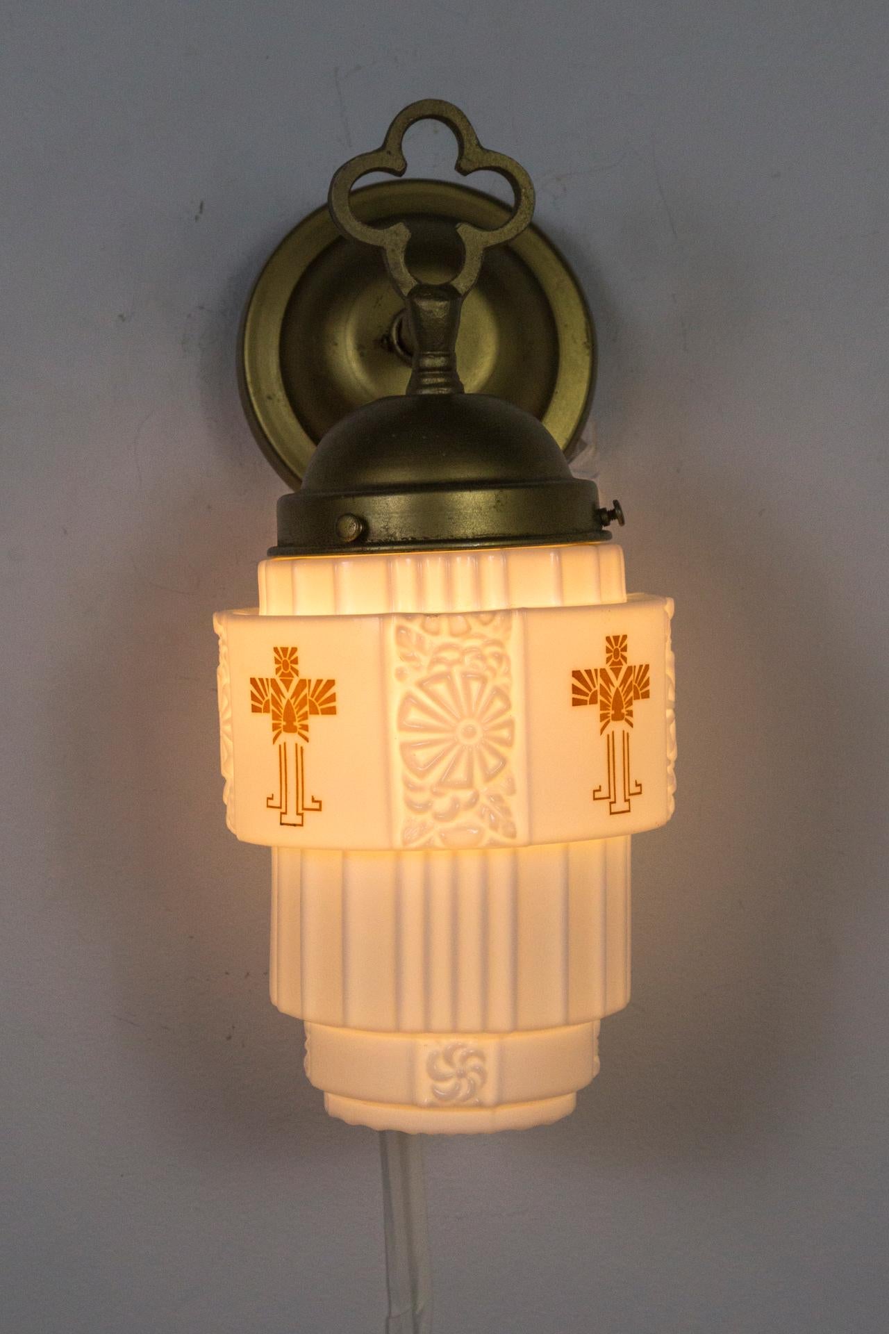 A pair of stepped, cylindrical, moulded, milk glass wall lights with gilded caps topped with a quatrefoils. Gothic influenced Art Deco pieces with imprinted flowers and printed crosses from the 1920s. 13.5 height x 8