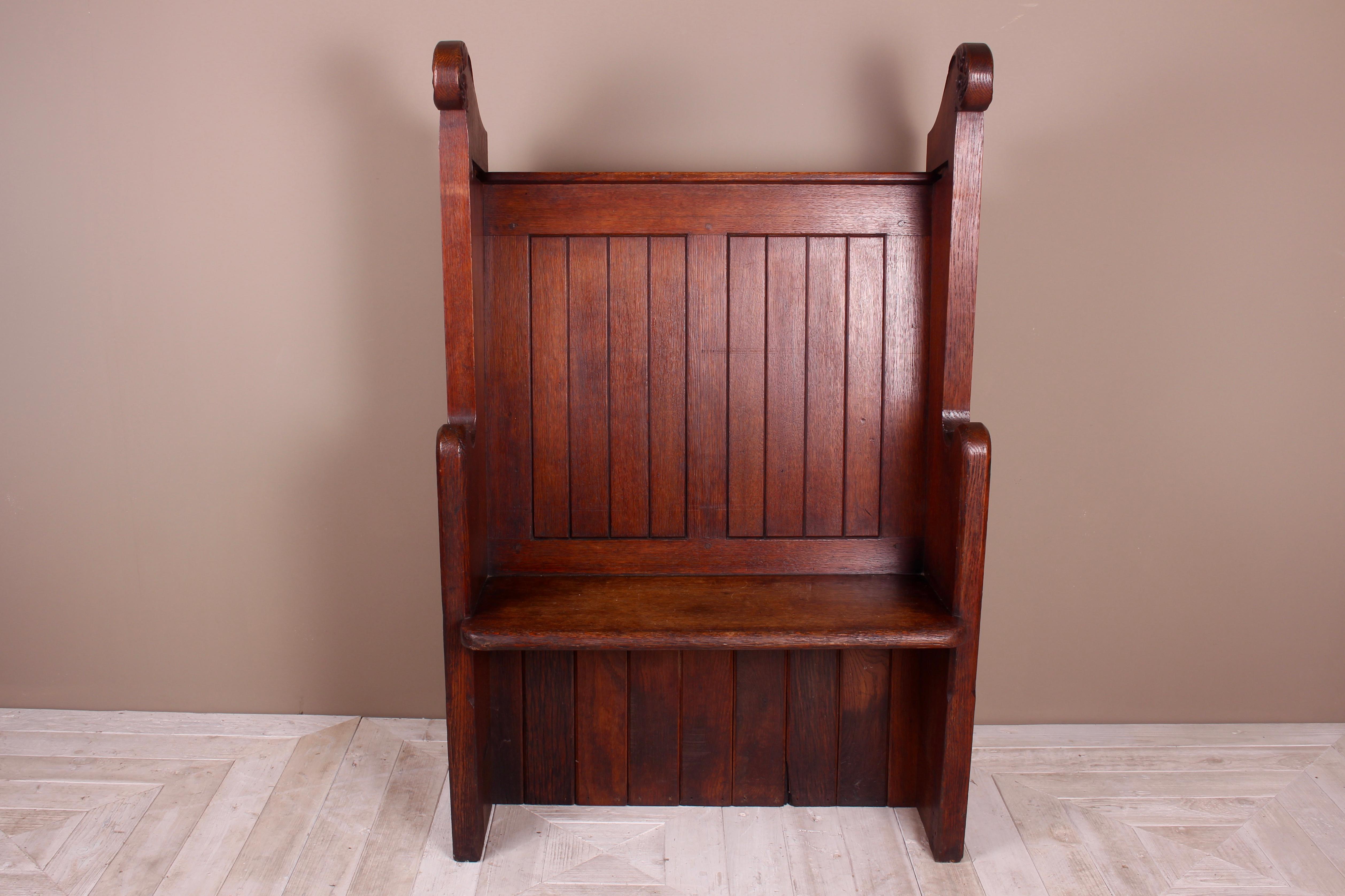 A lovely solid oak hall seat in the Gothic taste. Tongue and groove seat back flanked with nicely carved pew ends with church window tracery, topped with carved floral scrolls.