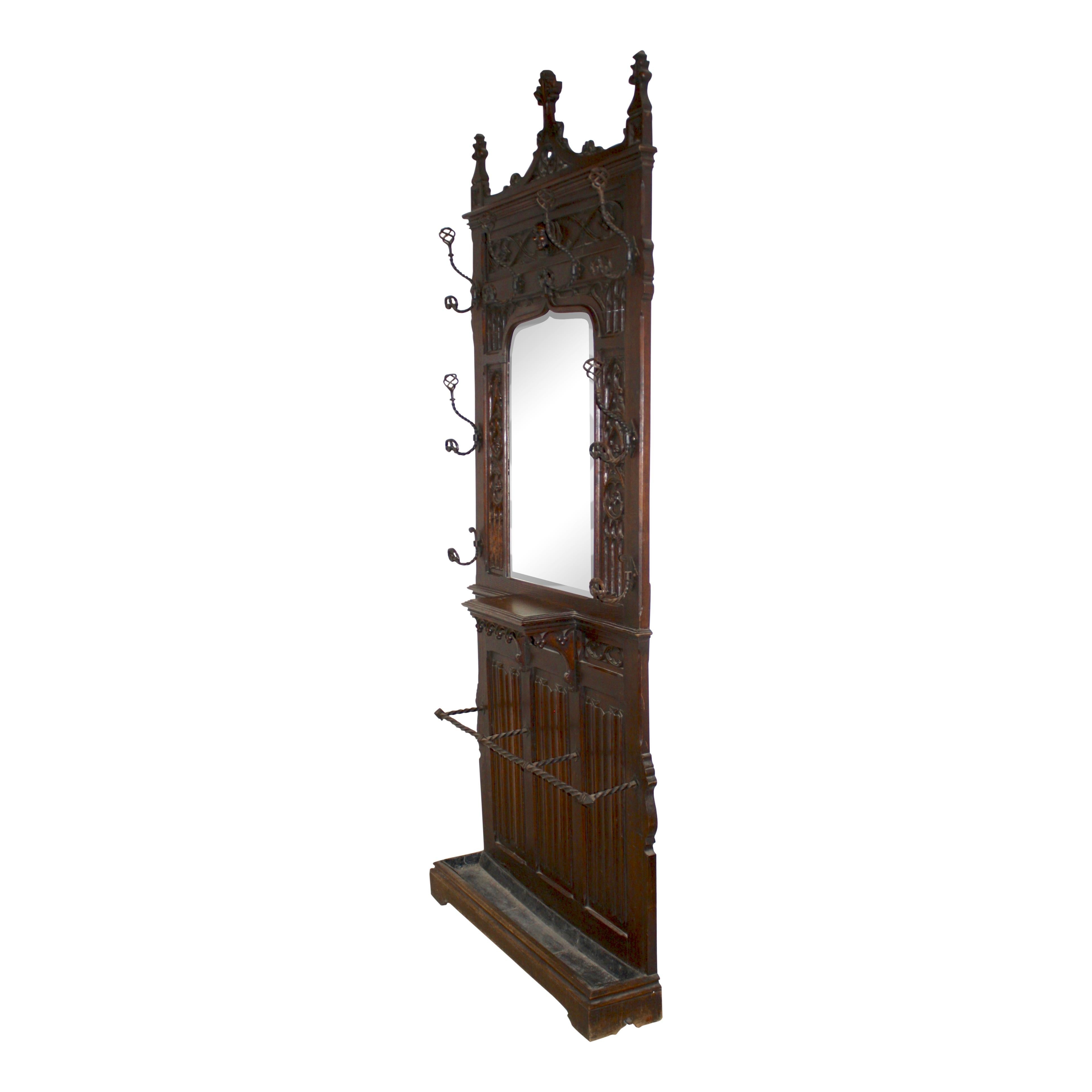 Standing just over eight feet tall, this oak hall stand makes an impressive statement. It features high relief carvings, six double wrought iron hooks, two single wrought iron hooks, a carved head protruding over a shaped beveled mirror with