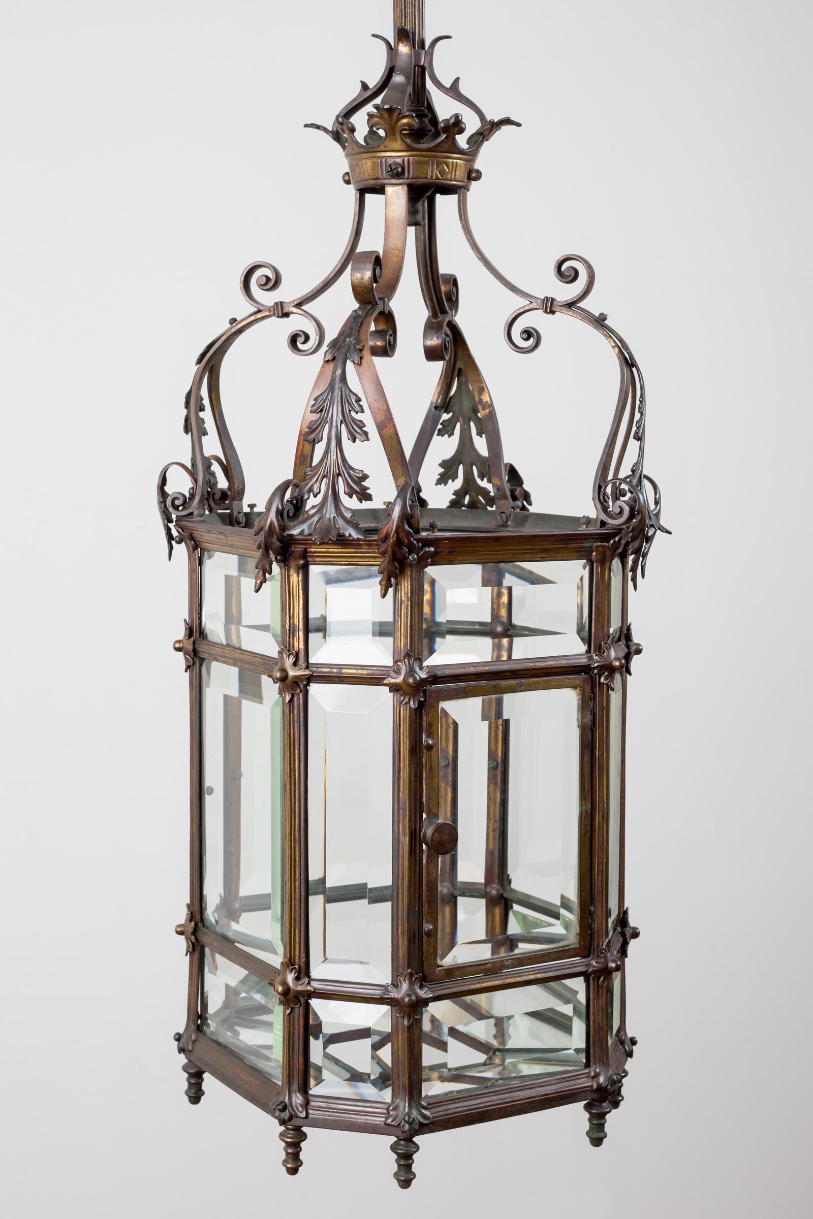 Gothic reform bronze octagonal partially gilded lacquered lantern with beveled glass plates and a surmount of C-scrolls, open scrolling leaves, topped by a crown. The original long reeded hanging rod can be cut to any length.
It has been