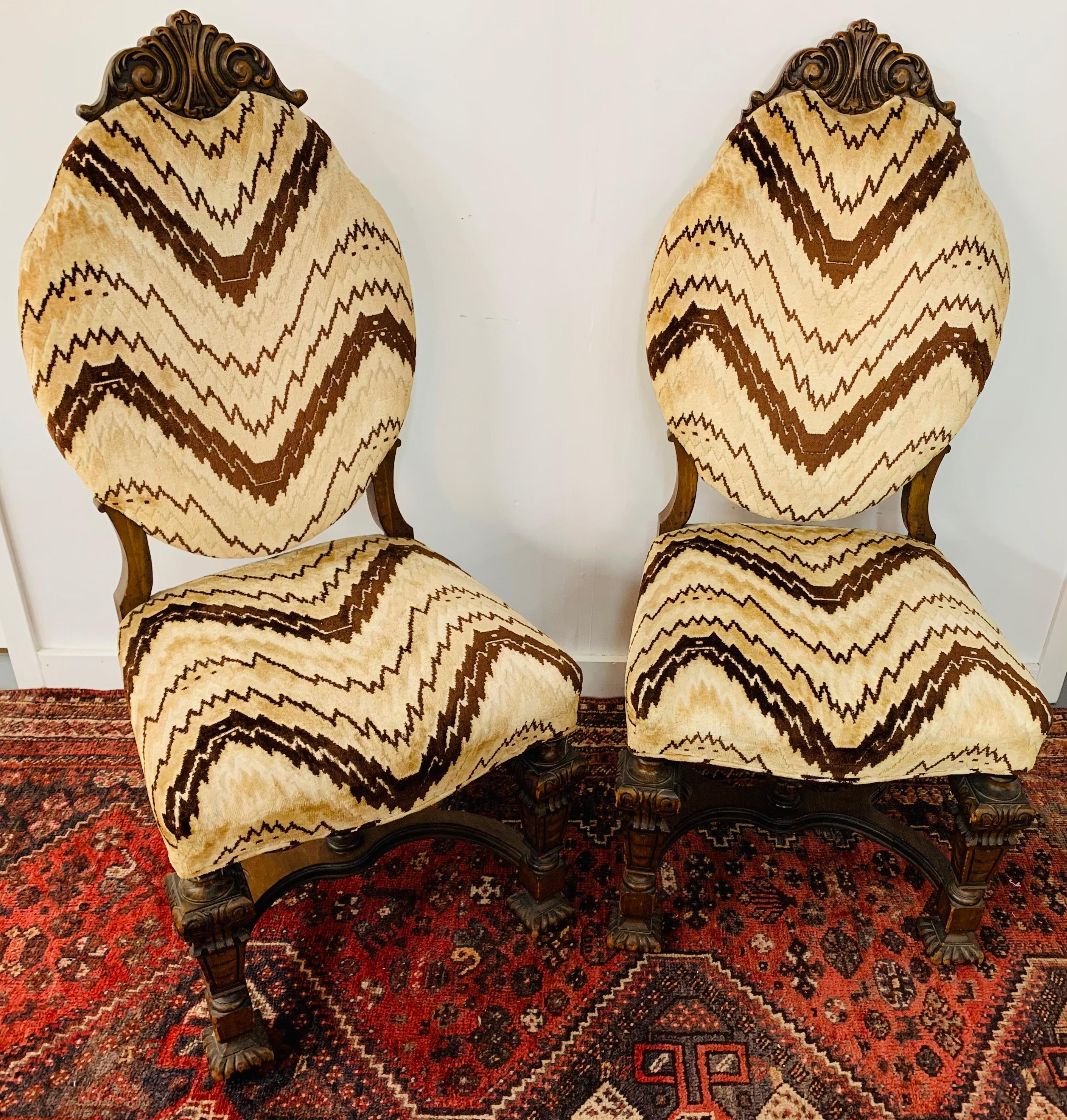 A unique pair of early 20th century gothic renaissance side chairs featuring boldly carved paw feet and original chevron striped upholstery in a classy beige and brown. The chairs are finely hand carved of oakwood and display classy craving