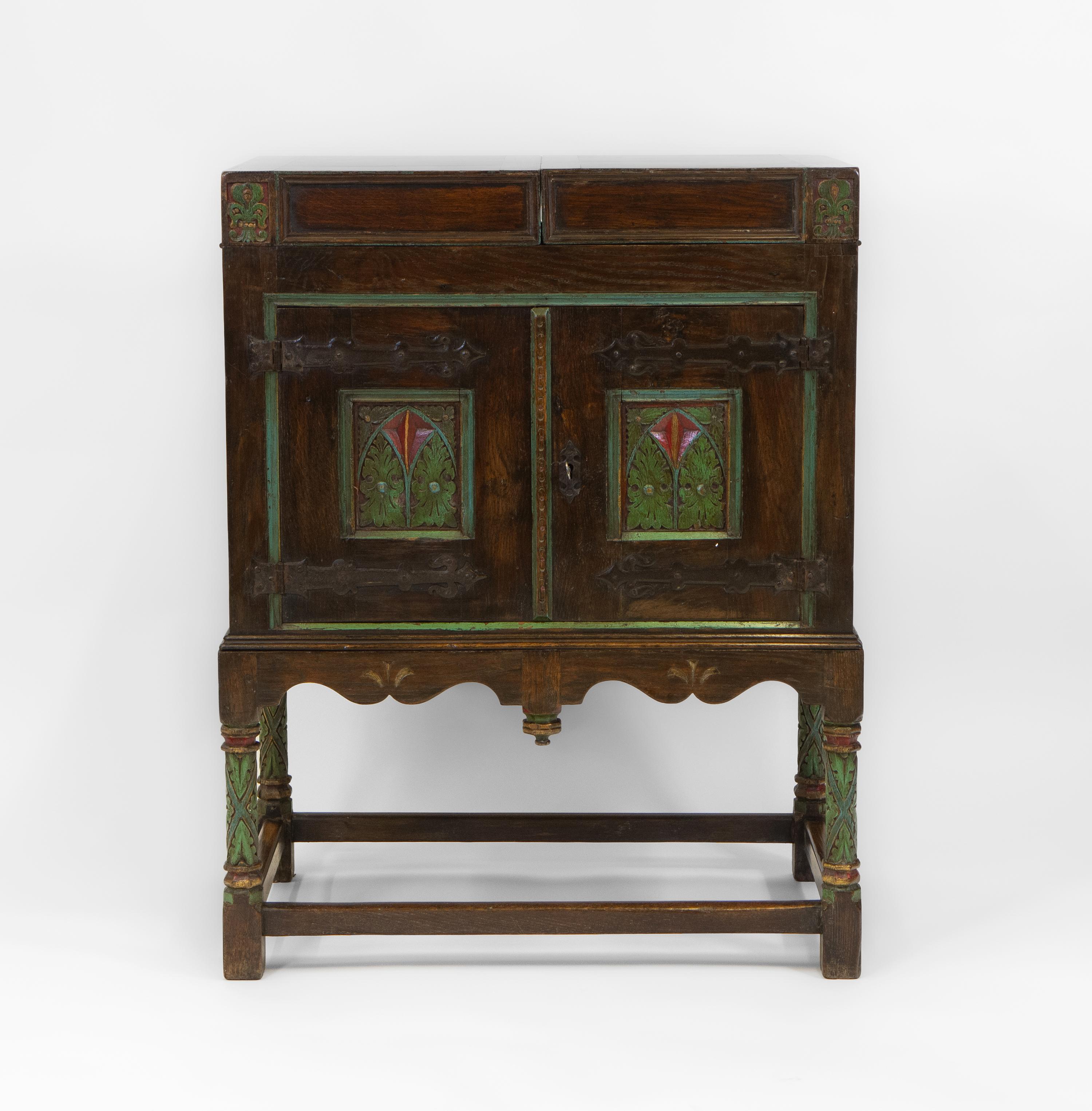 An interesting Gothic Revival / Arts & Crafts oak & polychrome painted cabinet. English. Circa 1920’s. 

Perfect for use as a drinks cabinet, the storage compartment on top neatly folds out, allowing for room to stand bottles and glasses etc.

Made