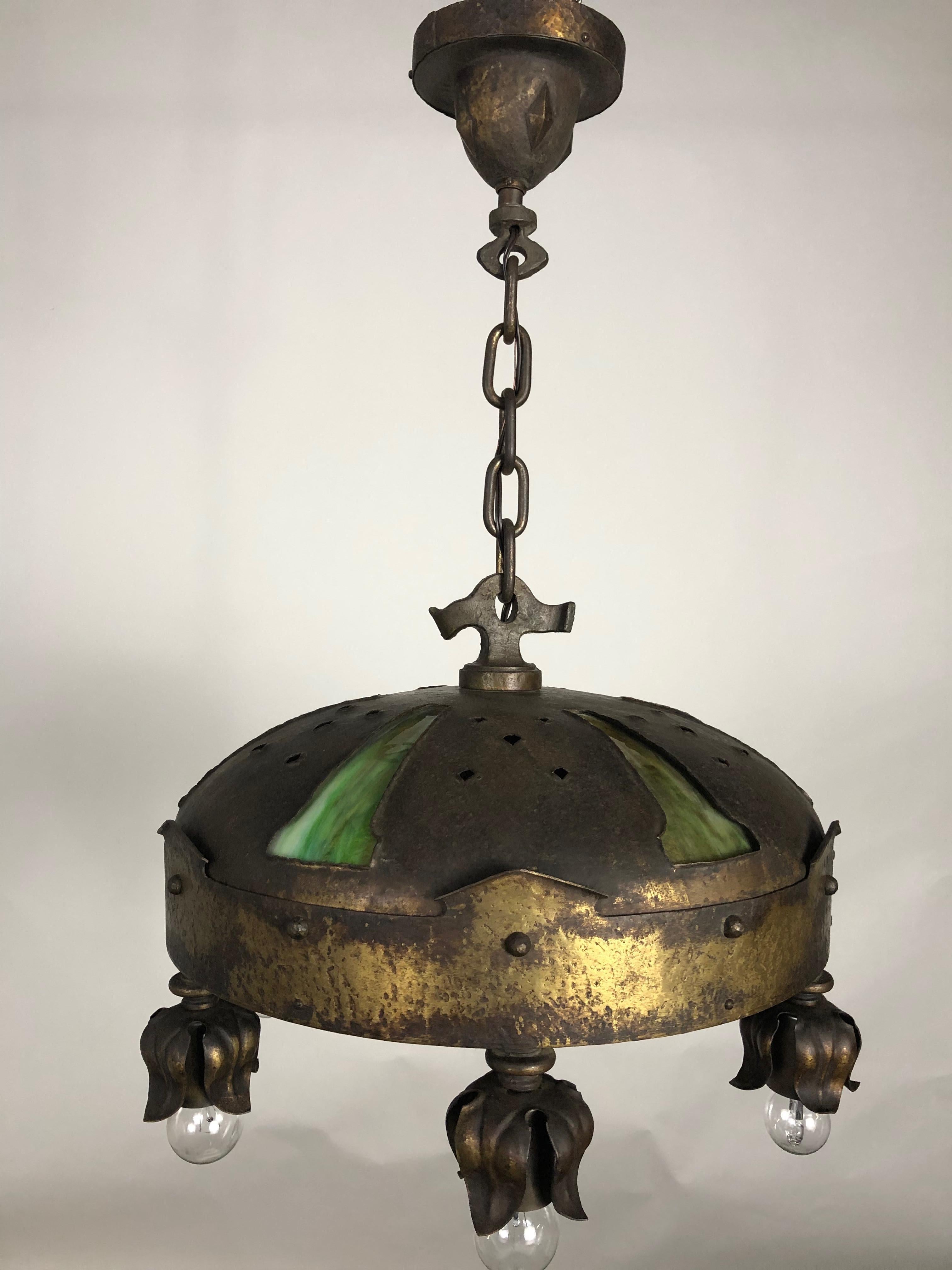 Early 1900s Gothic Revival Arts & Crafts handwrought and hammered fixture. This brass, steel and art glass pendant chandelier features over-sized rivets and six lights with foliage draped socket covers surround. A seventh-light is centered in the