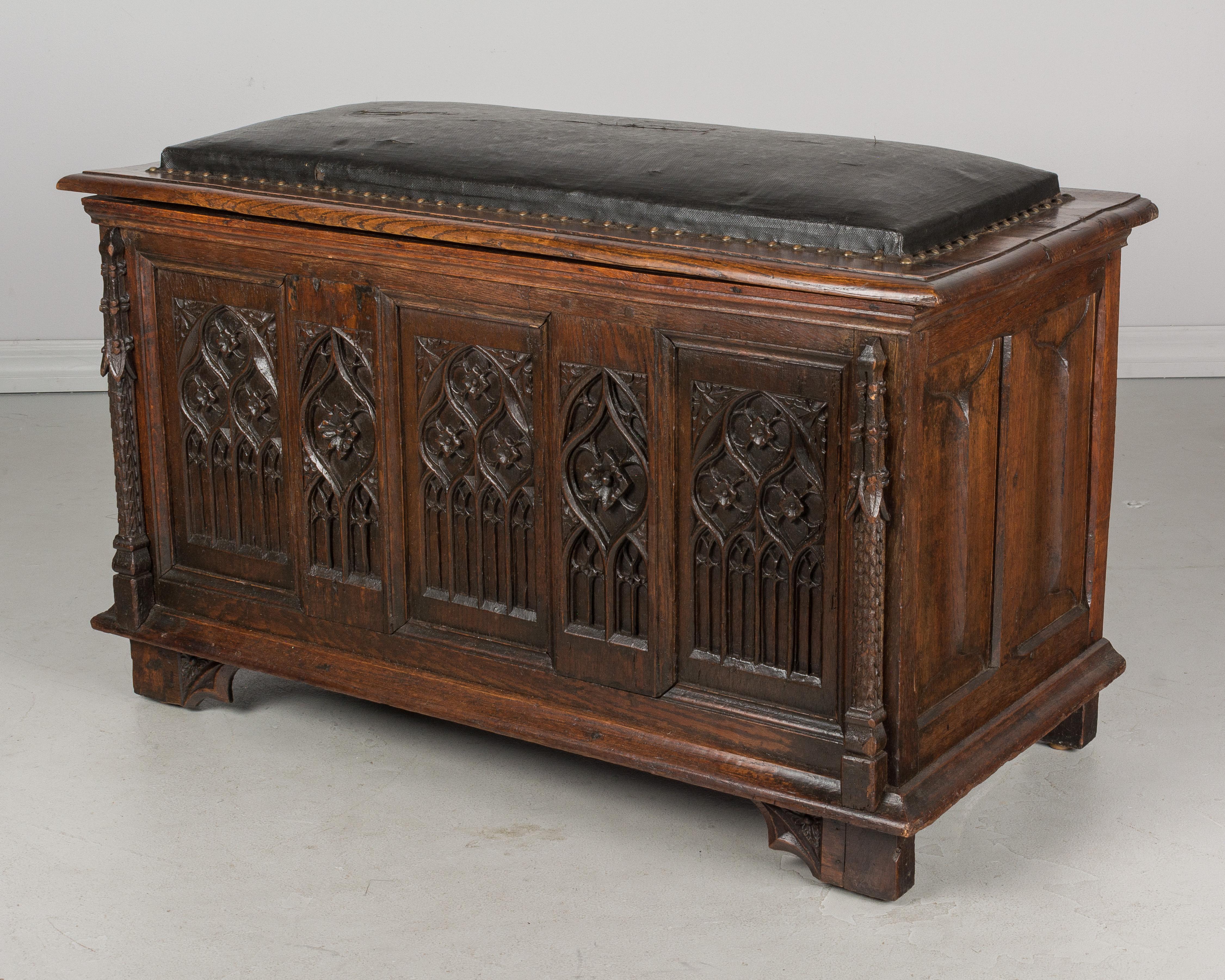 A 19th French Gothic Revival blanket chest, or bench, made of solid oak with hand carved architectural relief across the front. Black faux leather upholstered seat with nailhead trim. Waxed patina. A good solid trunk with ample storage. Perfect