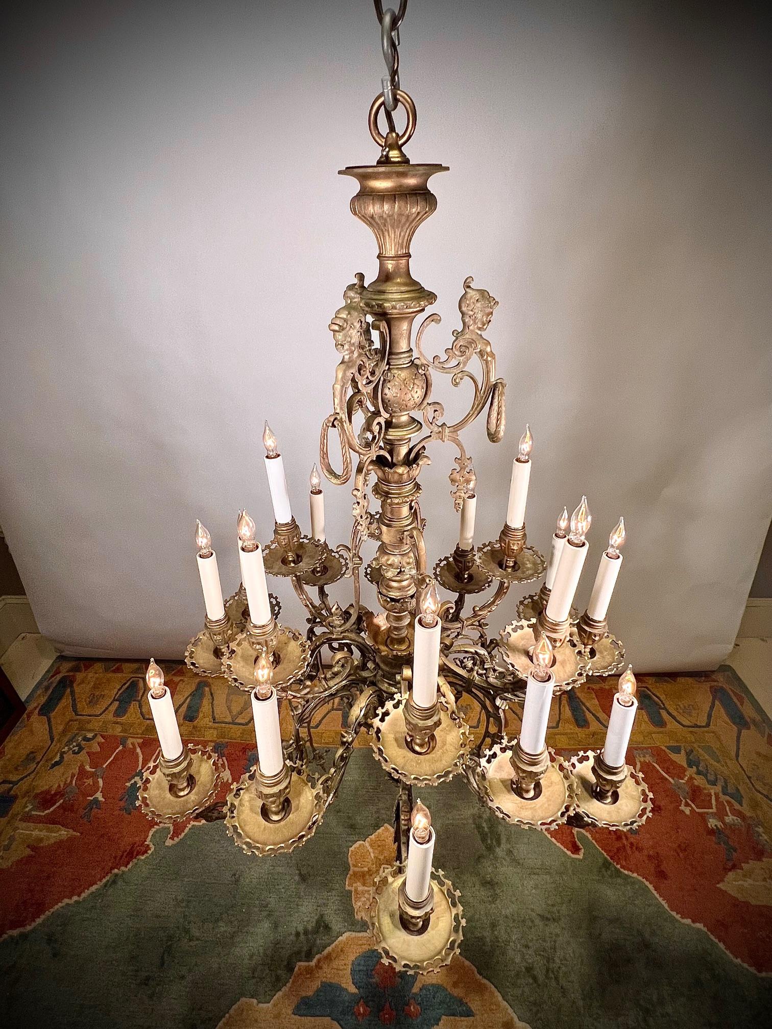 This chandelier is made of hand-cast brass in a design that is transitional from Gothic to Art Nouveau. While the bottom and arms have Gothic style elements, the female heads and scrolls at the top are more Art Nouveau. The  craftmanship, 18 lights,