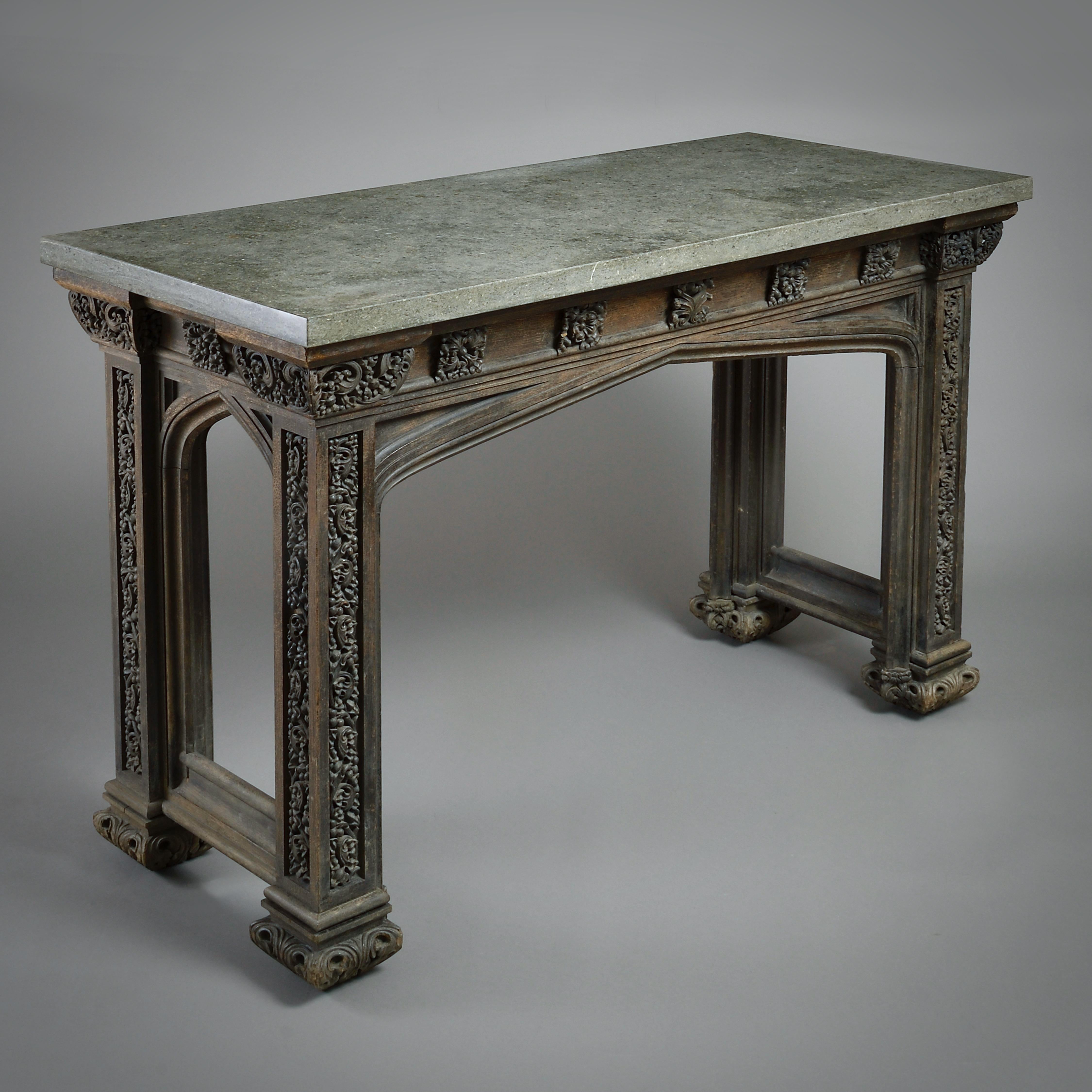 A FINE GOTHIC REVIVAL CARVED OAK SIDE TABLE POSSIBLY DESIGNED BY A.W.N. PUGIN, CIRCA 1835.

With later Purbeck fossil marble top. The moulded frieze applied with paterae, the panelled legs and capitals carved with scrolling foliage.