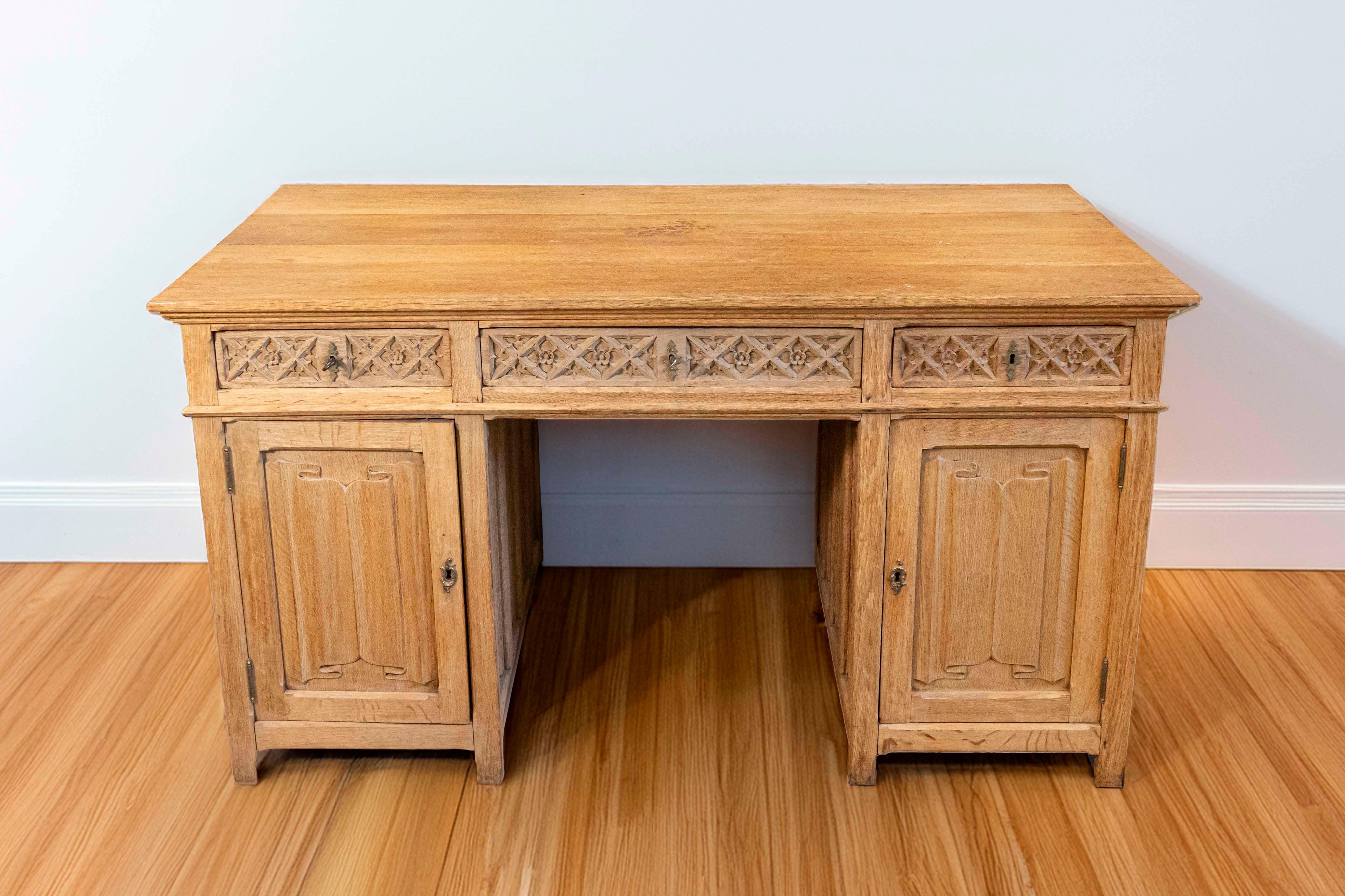 An English bleached oak Gothic Revival desk with linenfold motifs from the first half of the 19th century. This English desk features a rectangular top over three drawers and two side cabinets. The late Gothic influence, particularly praised during