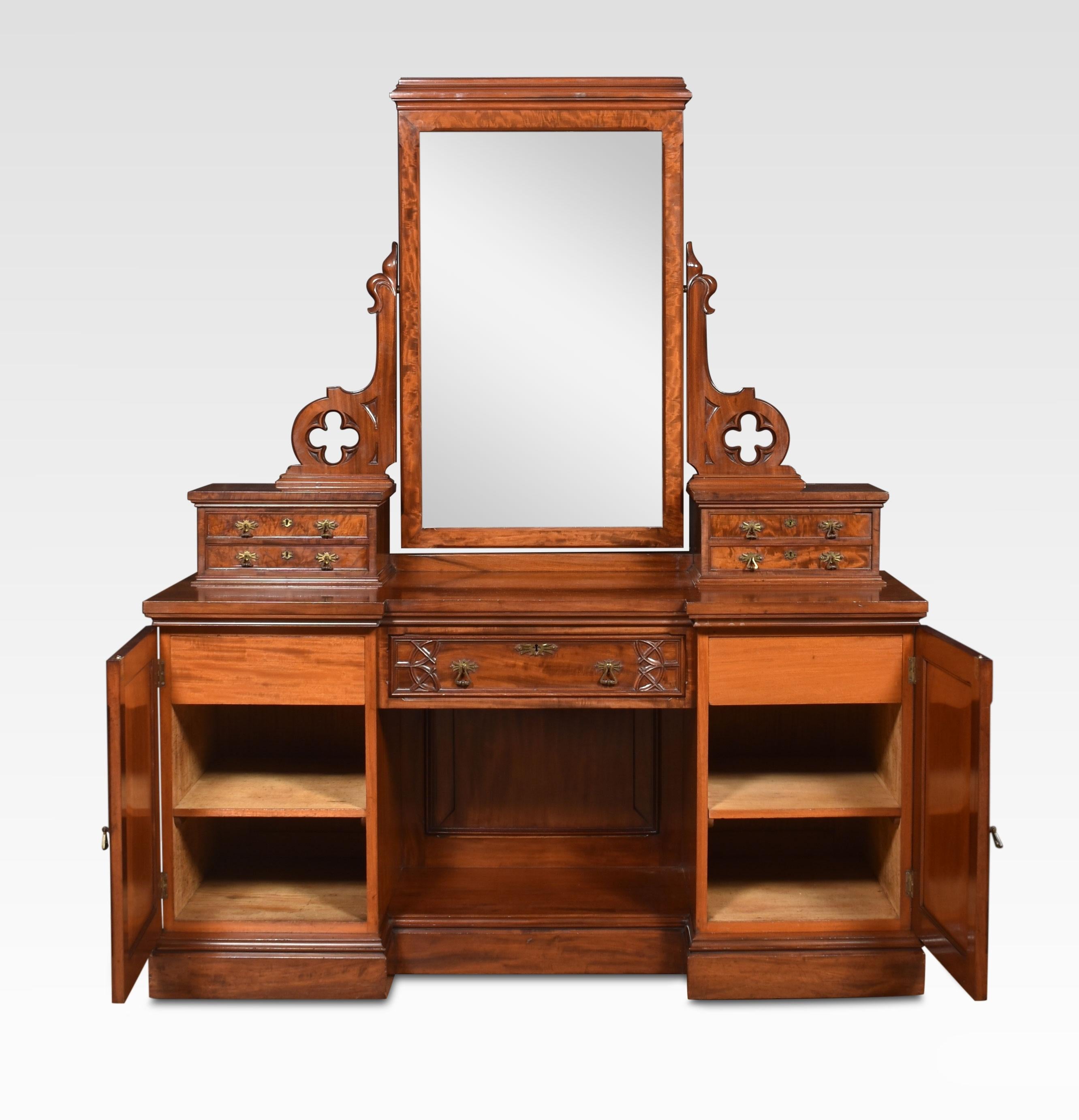 Gothic Revival dressing table, the rectangular mirror plate encased in moulded frame supported on stylised gothic arms above two banks of drawers. To the large rectangular mahogany top with a frieze drawer below flanked by cupboard doors. Al raised