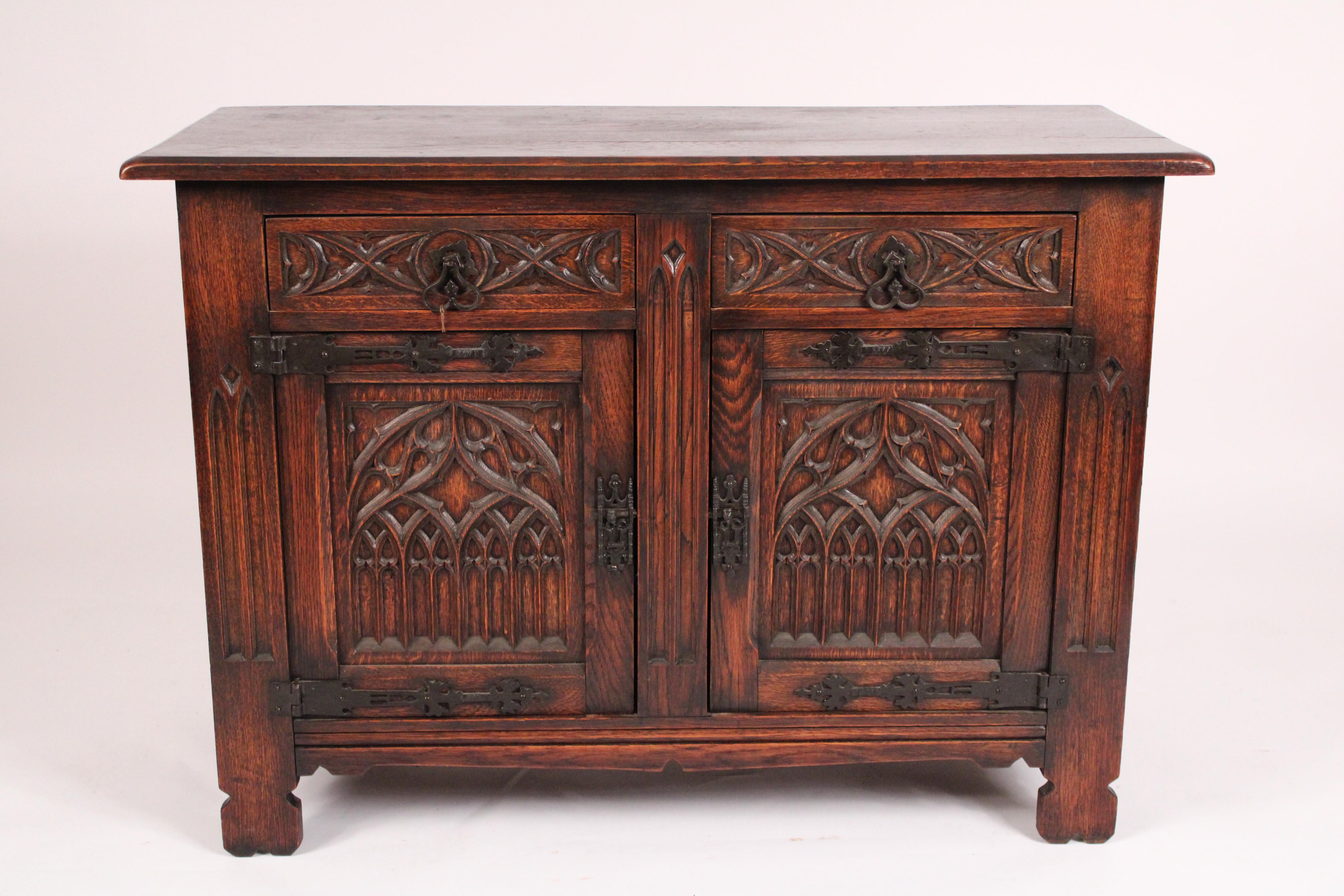 Gothic revival oak cabinet, circa 1920. With a 3 board top with beveled edges, two drawers with gothic tracery and iron pulls below are two doors with gothic arches the doors have interesting gothic style iron hinges, stiles on either side of doors