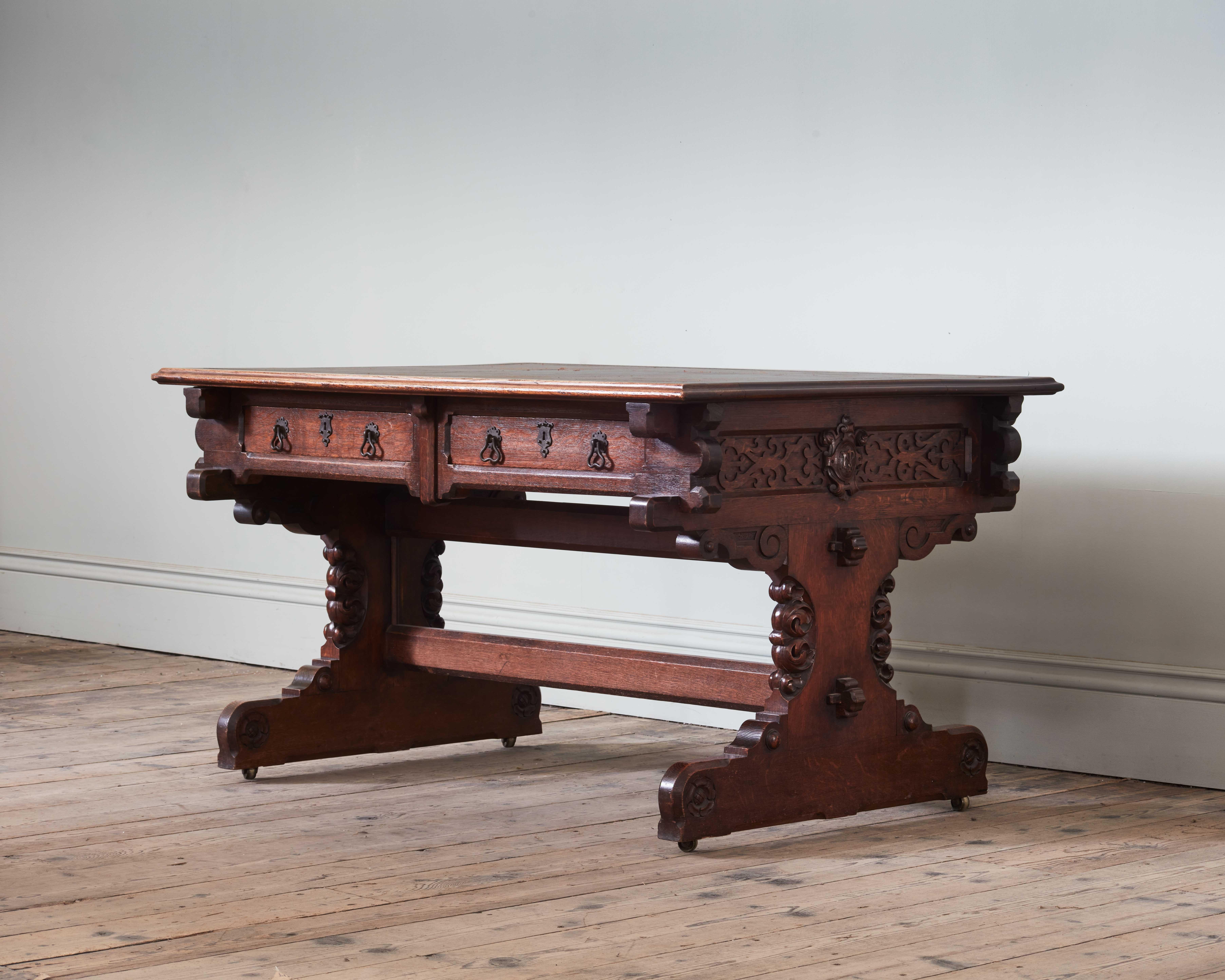 A Gothic Revival Oak Writing Table by J. G. Crace, after a design by Pugin

With extensive gothic carving work, the sides with strapwork carving centred by a monogram reading “MP”, the trestle ends joined by two stretchers and raised on brass
