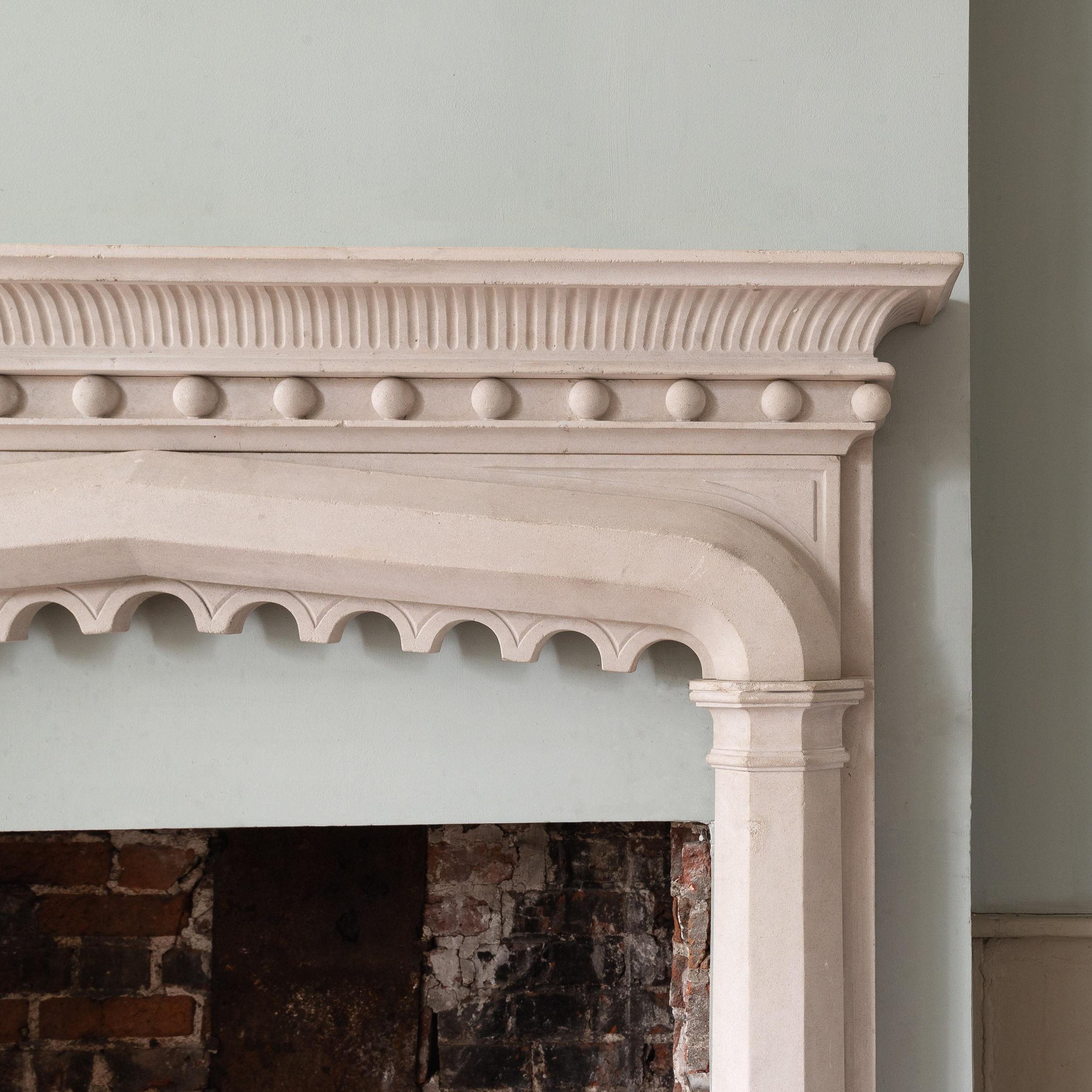 A Gothic revival Portland stone chimneypiece, modern, in the late eighteenth to early nineteenth century style, the shelf with convex fluted under-mould and a repeating band of spheres below, the surround composed of octagonal pilaster jambs spanned