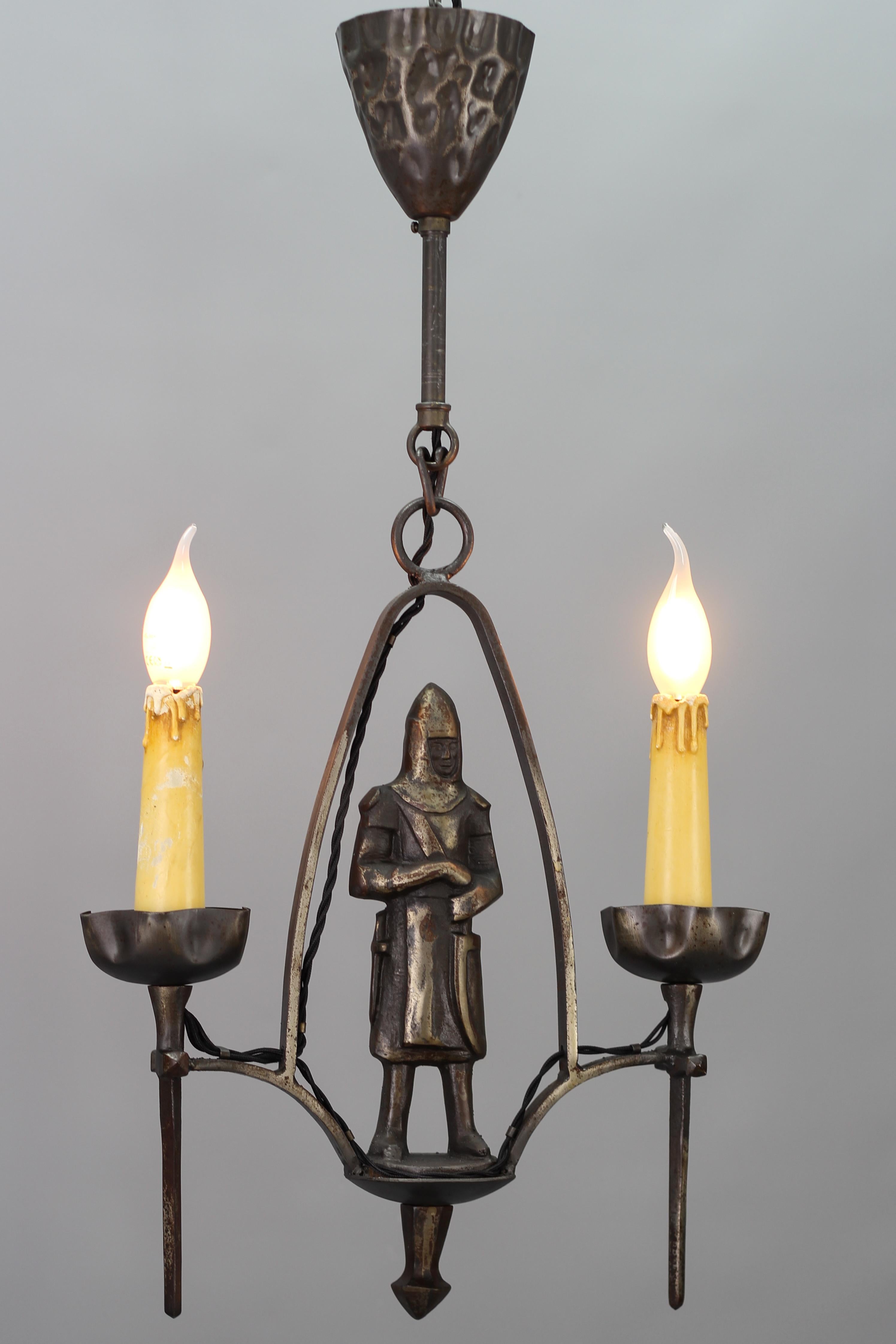 Gothic Revival style wrought iron and metal two-light chandelier with knight, France, circa the 1950s.
This amazing wrought iron and bronzed metal pendant chandelier features the figure of a knight in the center of the light fixture and two arms in